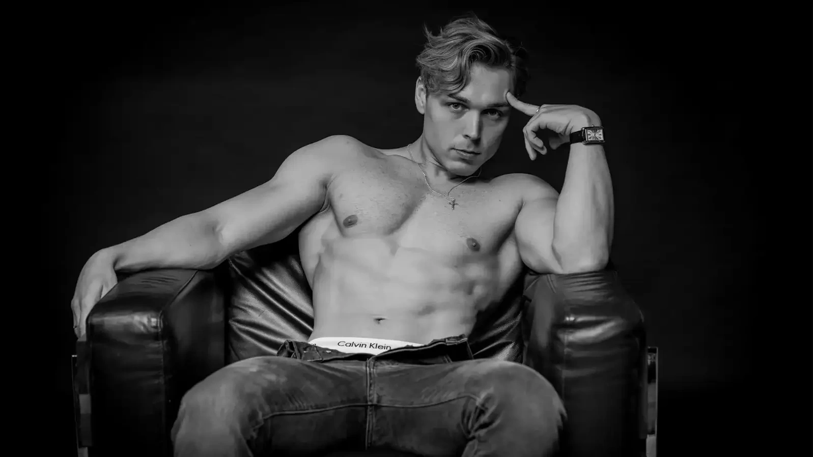 Black and white physique portrait of a man seated in a leather armchair, low-key studio lighting — studio portraits and headshots in Leeds at Dock Street Studio