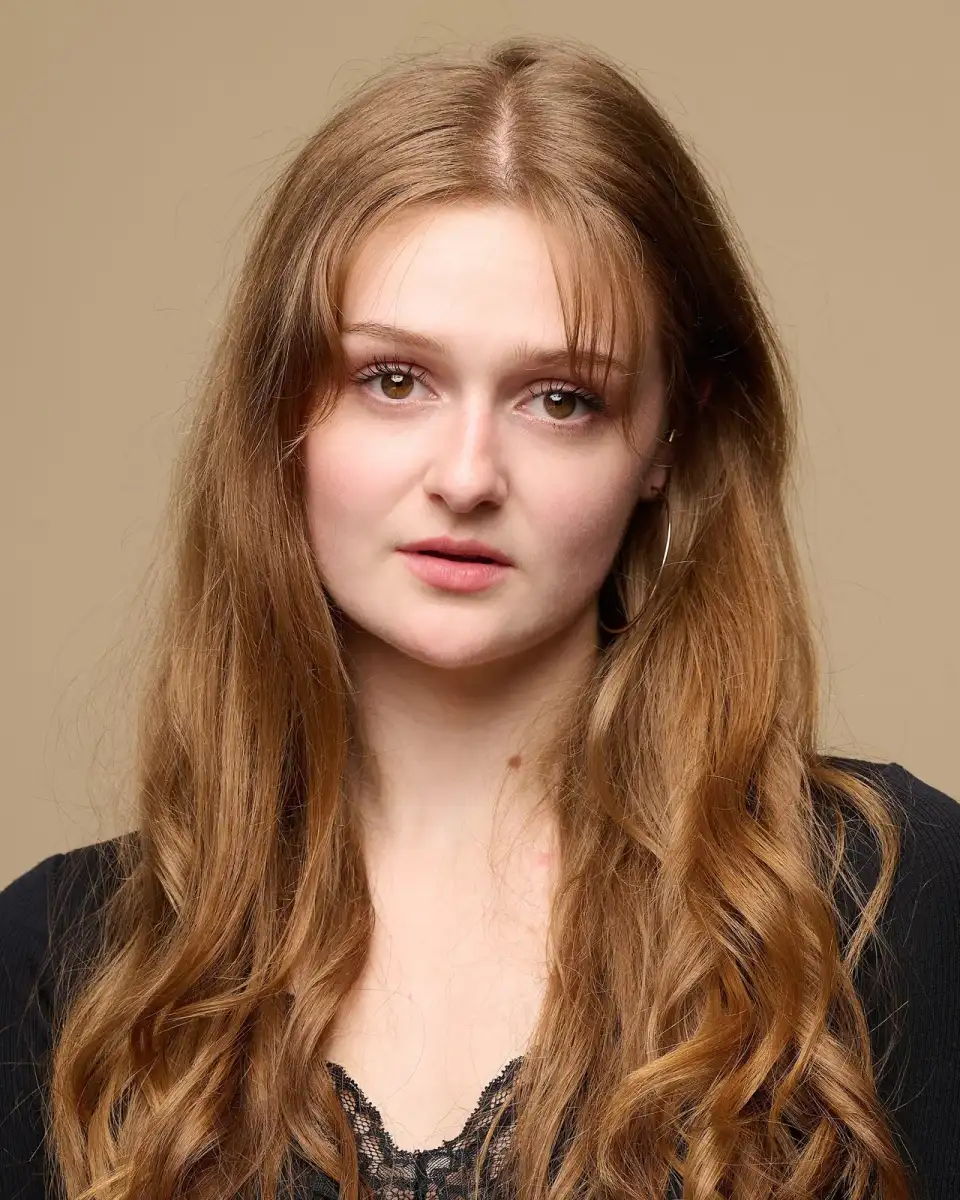 Straight-on actor headshot of a young woman with long auburn hair in a black cardigan and lace top on a sand backdrop — Spotlight actor headshots in Leeds at Dock Street Studio