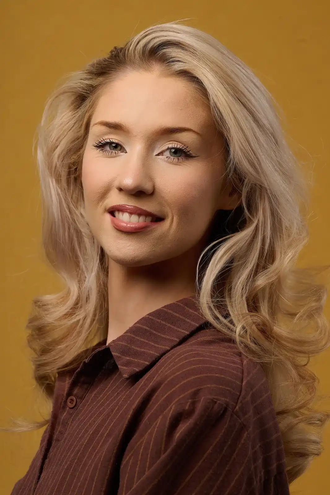 Smiling actor headshot of a blonde woman in a brown pinstripe shirt, shoulder turned to camera on a mustard backdrop — actor headshots Leeds, Dock Street Studio