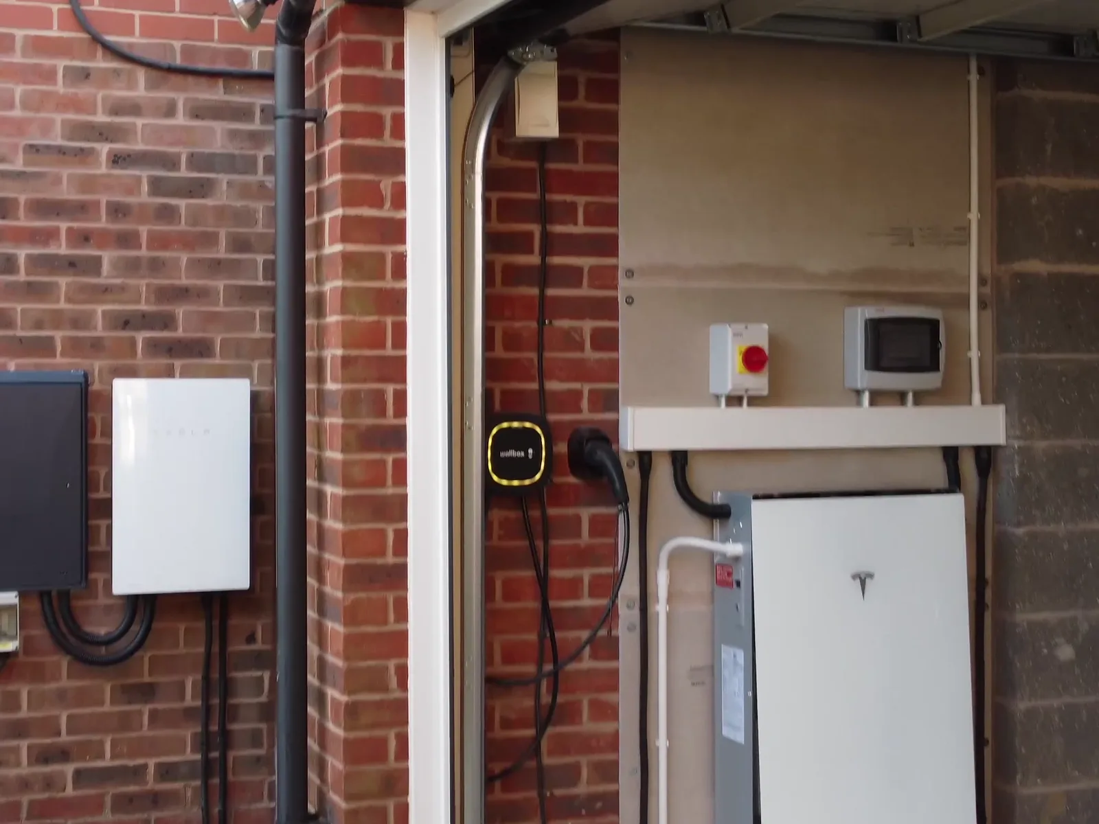 A Tesla Backup Gateway on the outside wall and a Powerwall and car charger in the garage of a home in Wymeswold