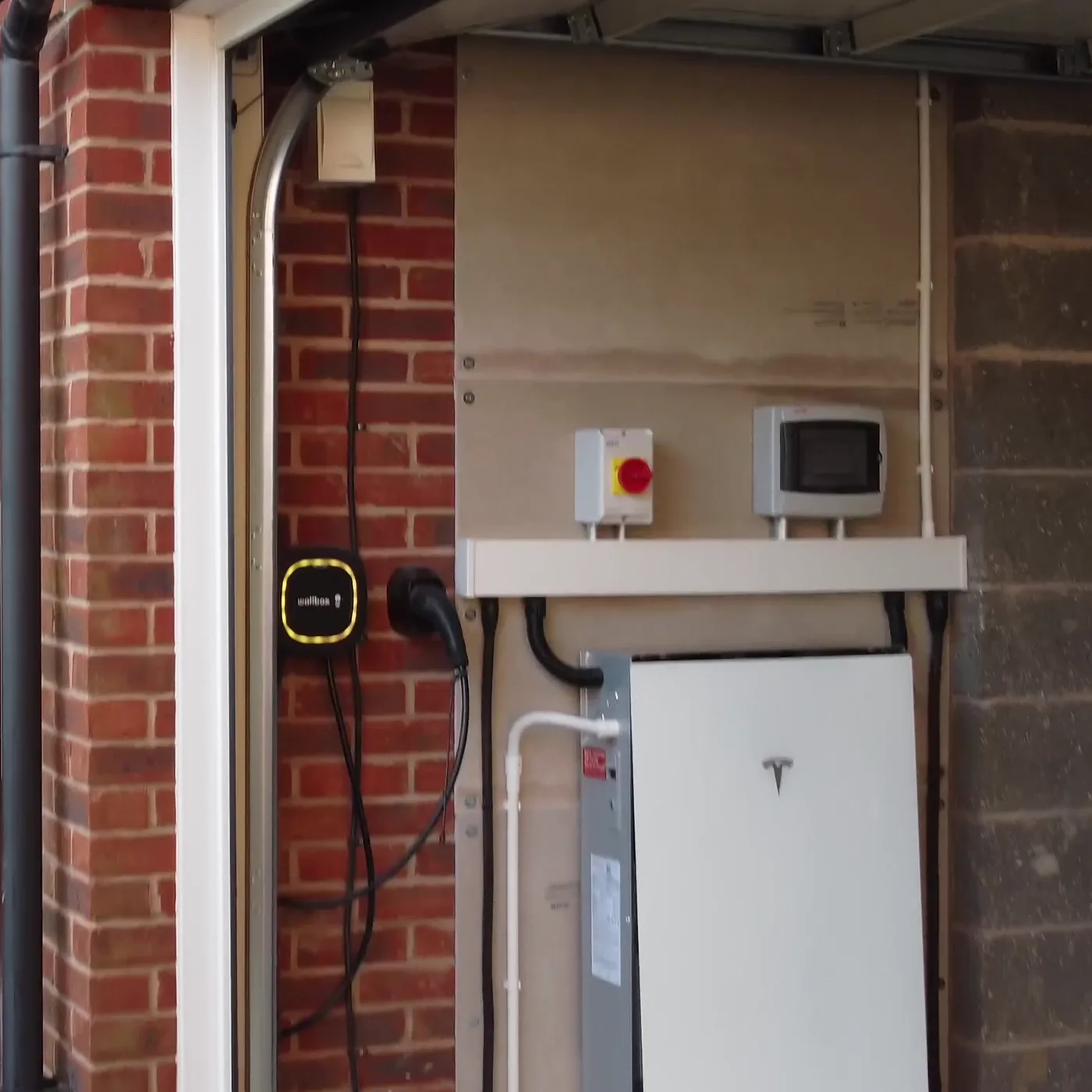 A Tesla Powerwall fitted in a garage in Wymeswold, with the car charger on the wall beside it