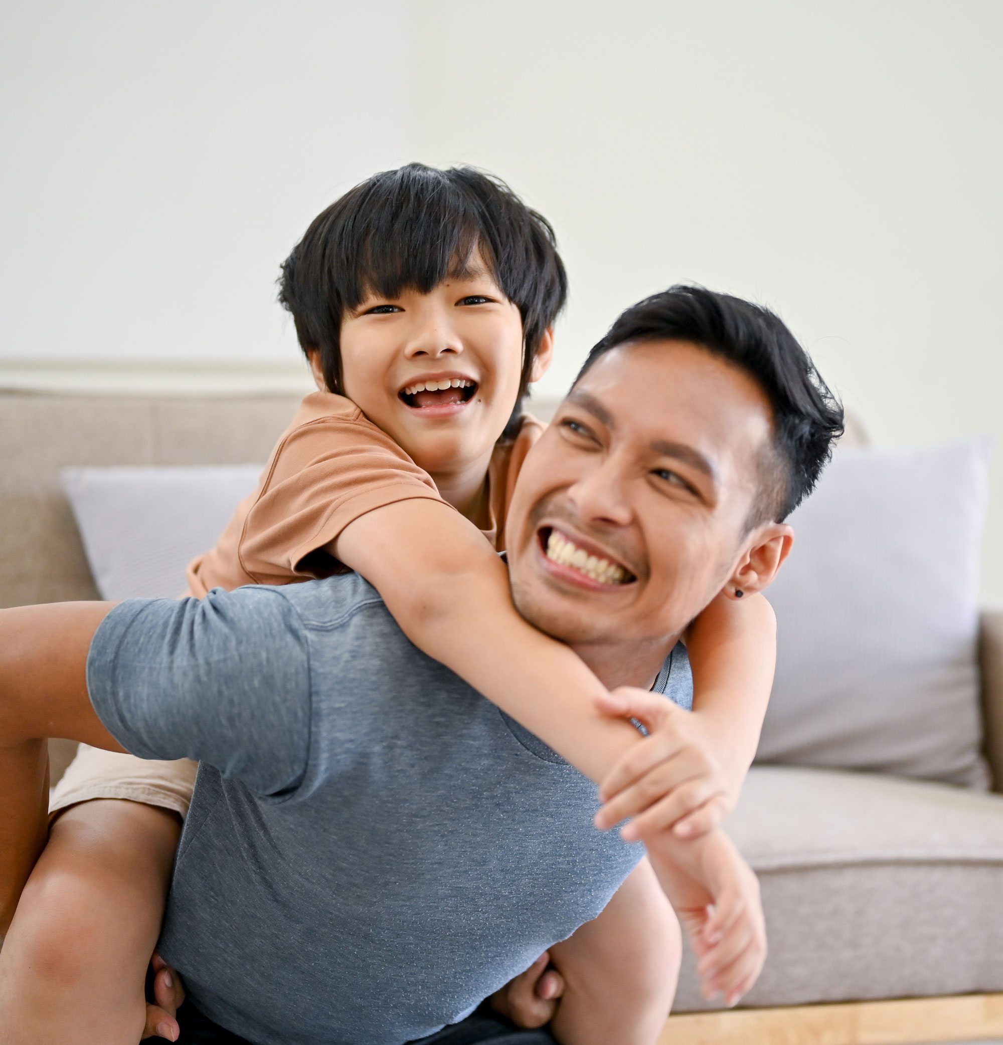 Smiling father giving a piggyback ride to his happy young son in a living room.