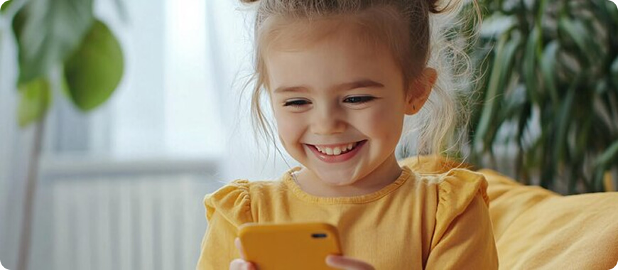 A happy child smiling while using a smartphone.