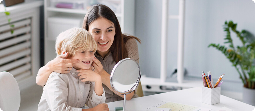 A teacher and a child practicing the 'TH' sound in front of a mirror