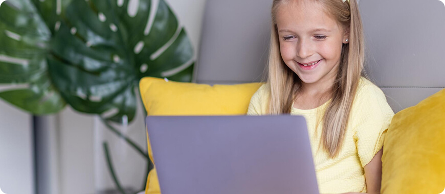 Niña feliz aprendiendo inglés en línea en su laptop – mejores sitios web gratuitos para niños practicar habla, lectura y gramática en casa en 2025