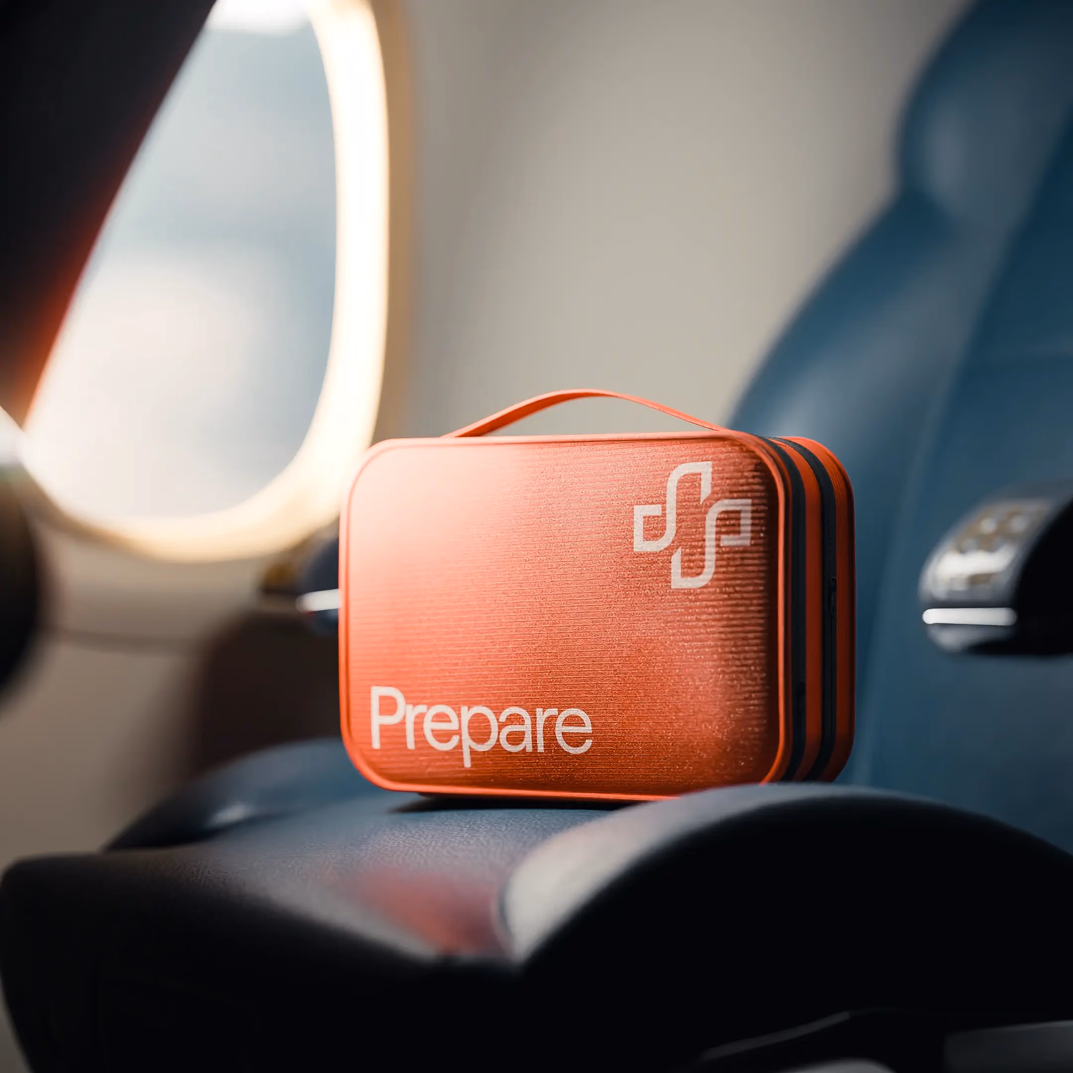 an image showing an orange first-aid kit on an airplane seat near the window