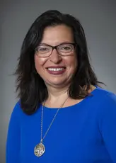 A woman with medium length dark hair and glasses smiling at the camera.