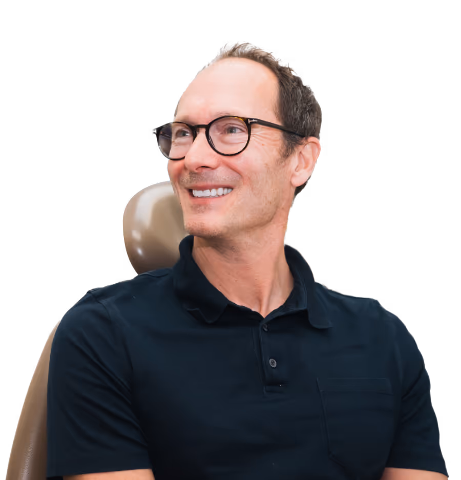 Smiling man wearing glasses and a black polo shirt sitting in a chair, looking to the side.
