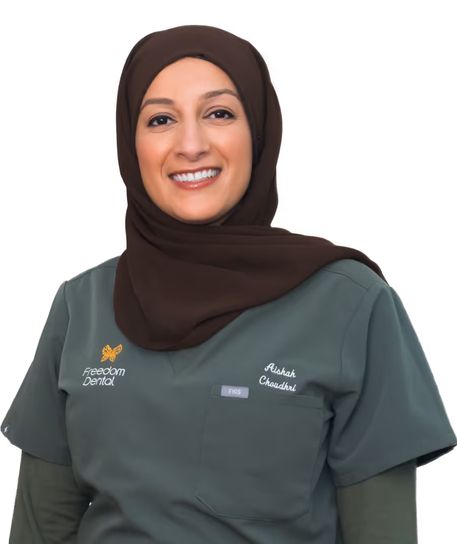 Smiling woman wearing a brown hijab and green dental scrubs with the name Aishah Choudhri and Freedom Dental logo.