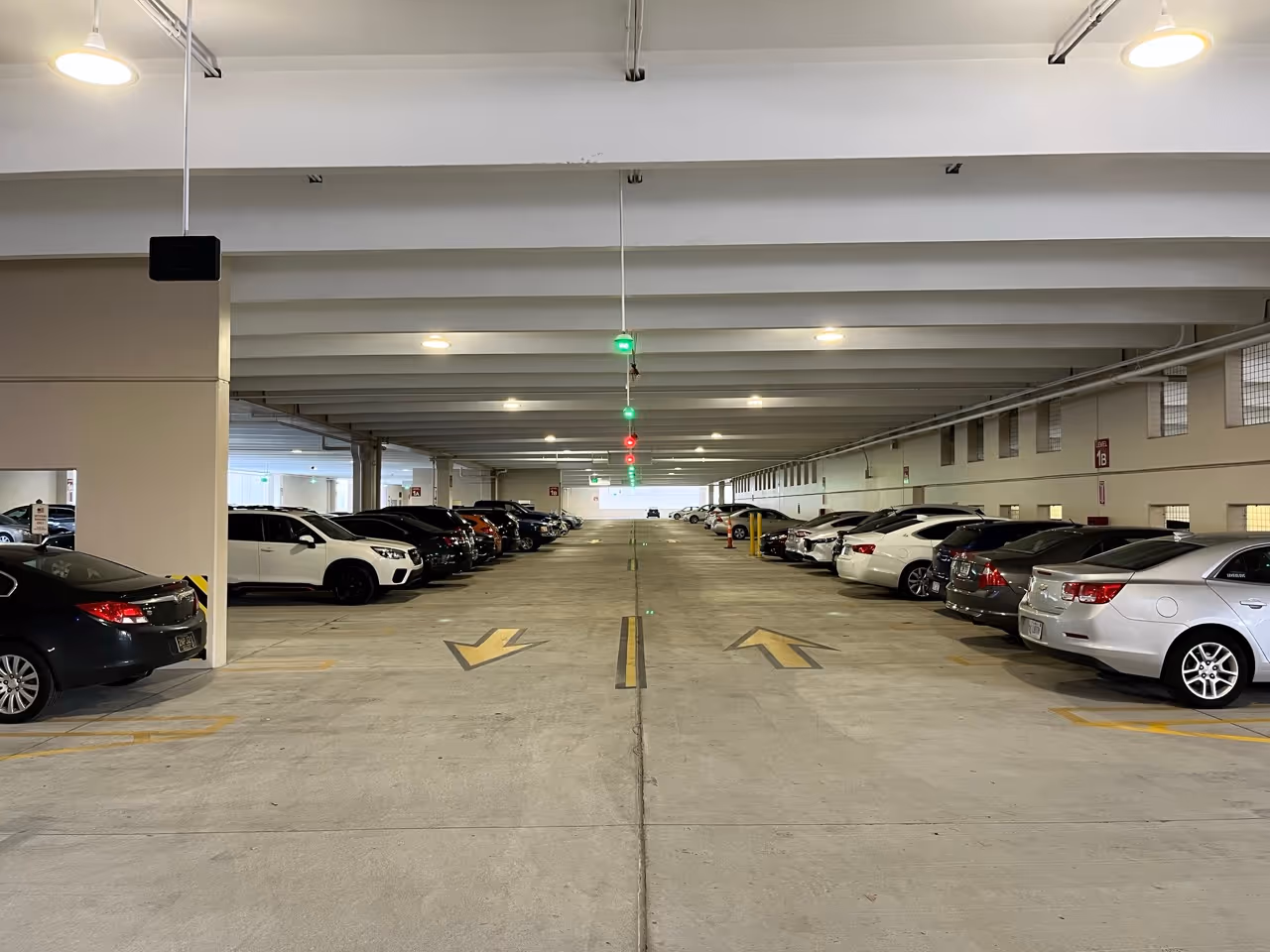 Indoor parking garage with cars parked on both sides and directional arrows on the floor.