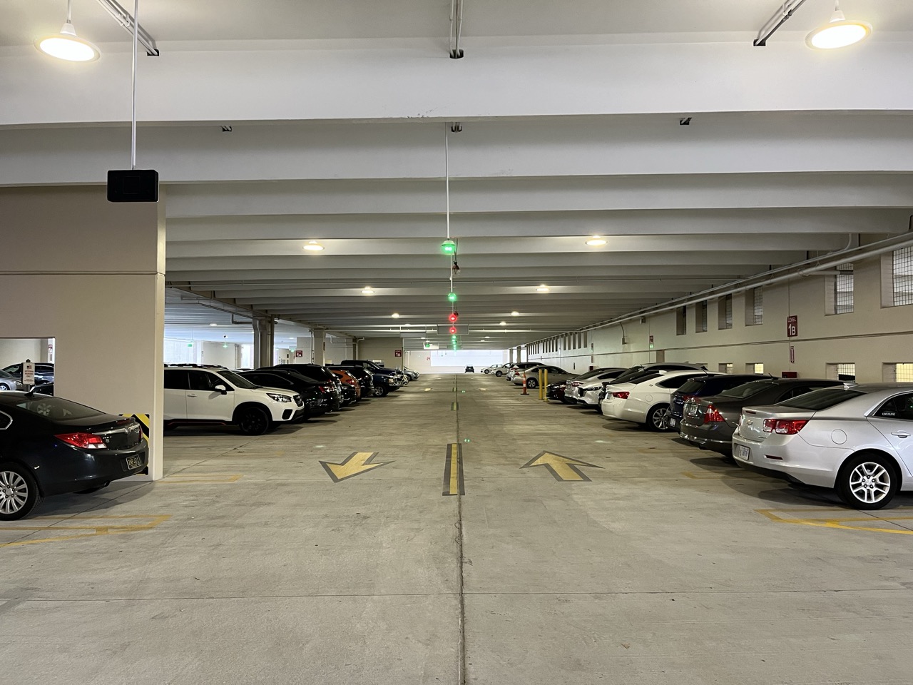 Indoor parking garage with cars parked on both sides and directional arrows on the floor.