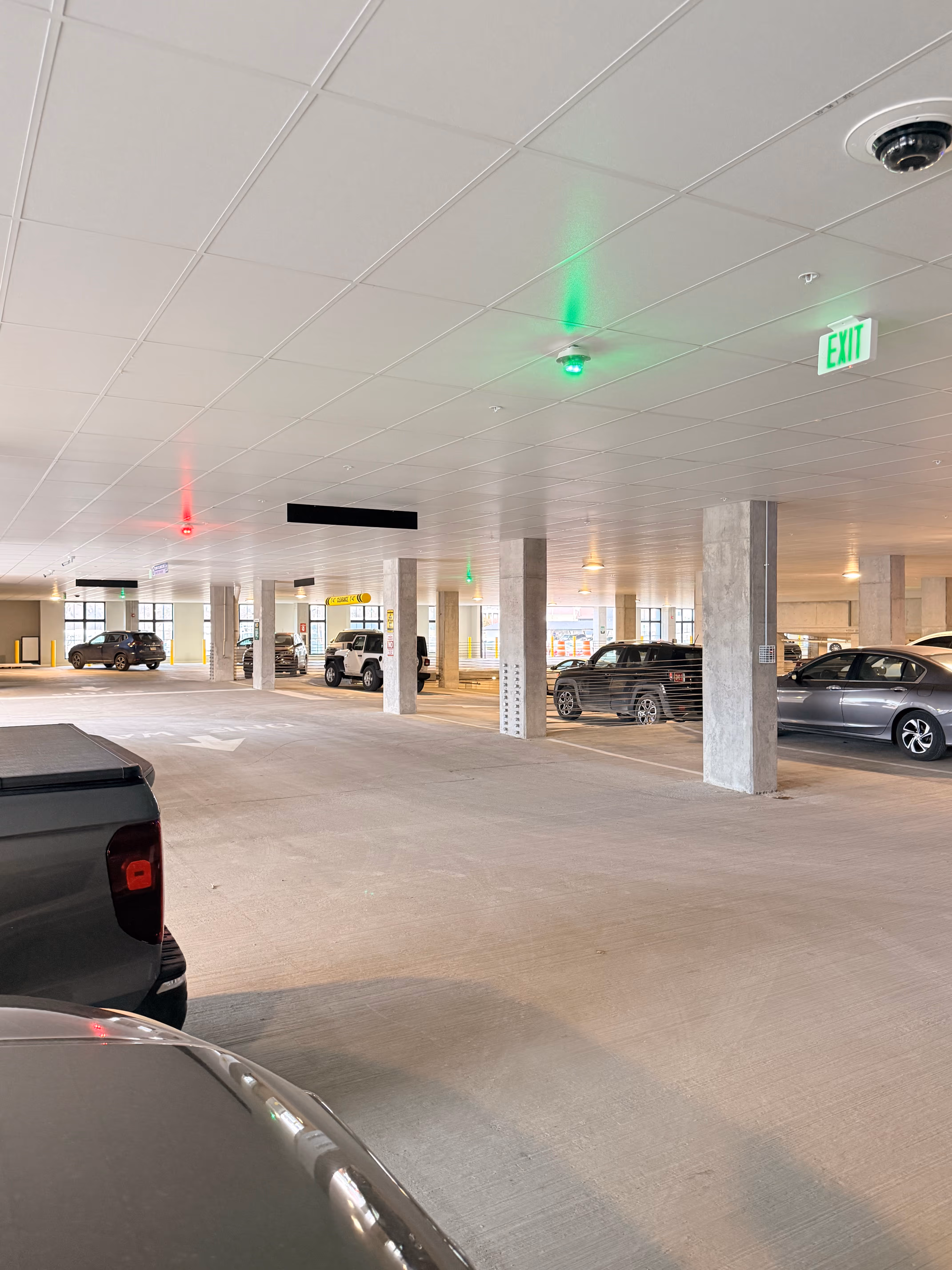 Indoor parking garage with cars parked on both sides and directional arrows on the floor.