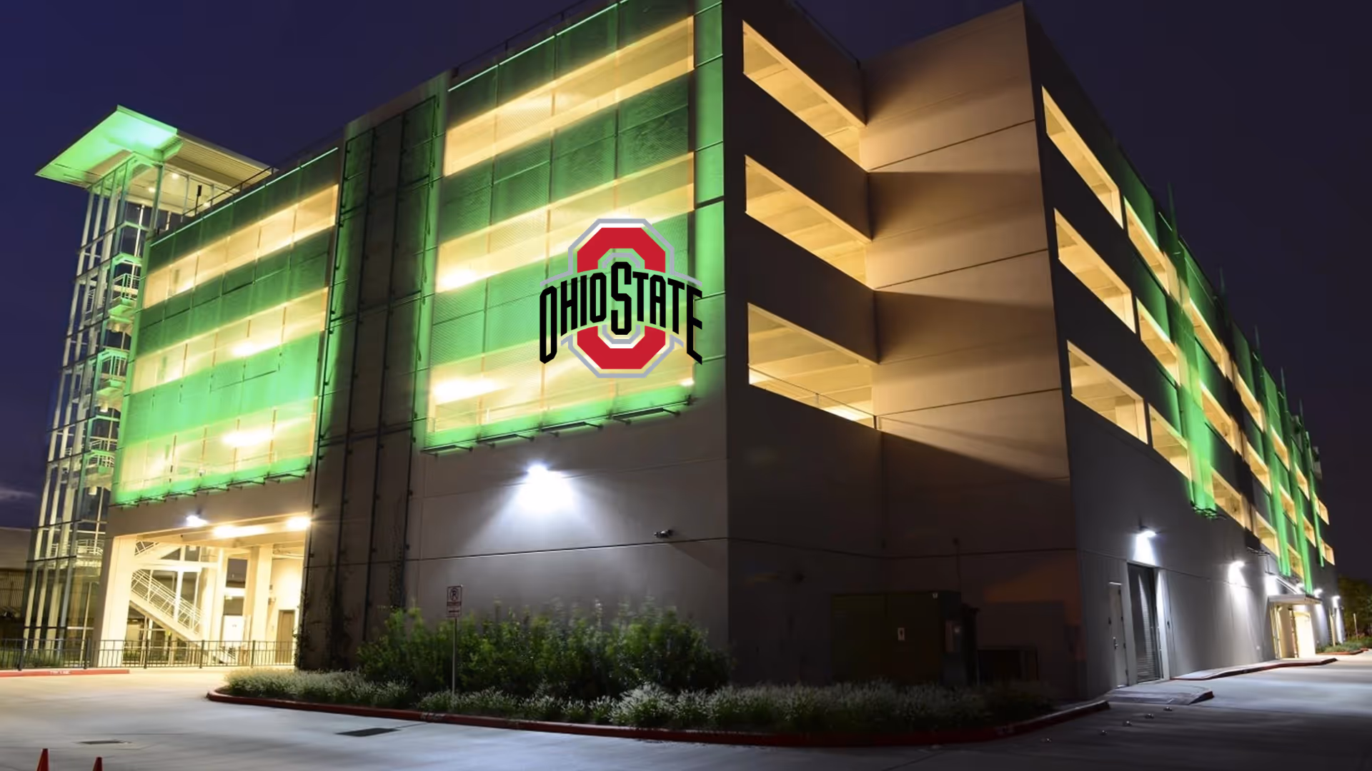Multi-level parking garage illuminated with green lights at night with Ohio State logo on side.