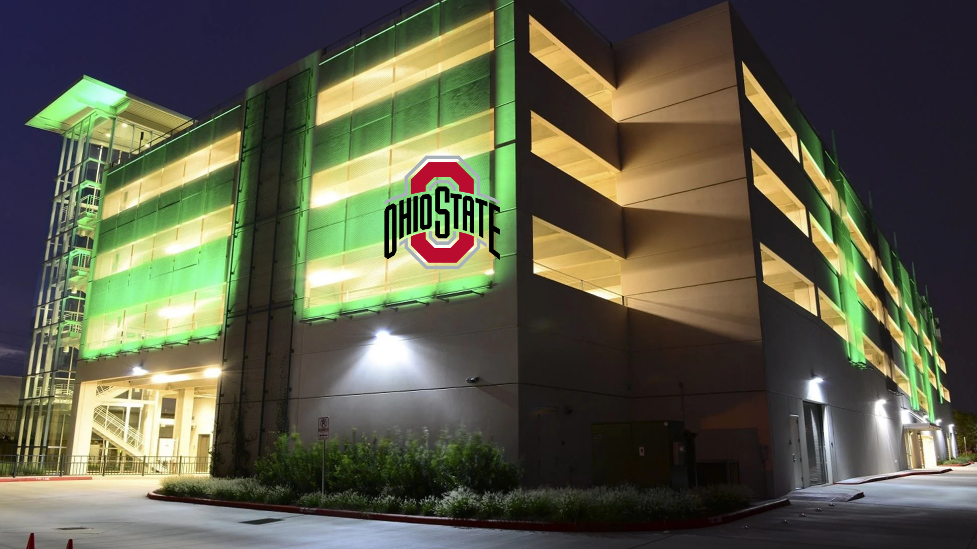 Multi-level parking garage illuminated with green lights at night with Ohio State logo on side.