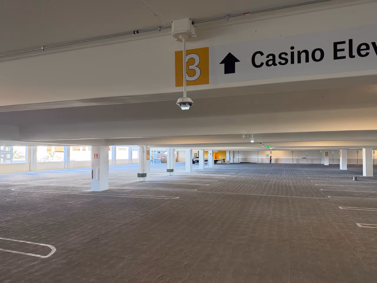 Empty multi-level parking garage with ceiling cameras and signs indicating floor 3 and elevator direction.