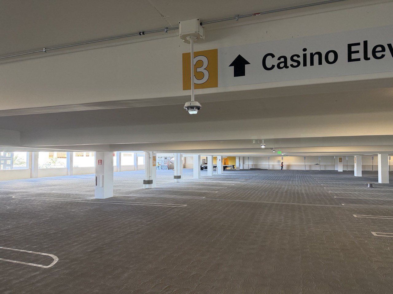 Empty multi-level parking garage with ceiling cameras and signs indicating floor 3 and elevator direction.