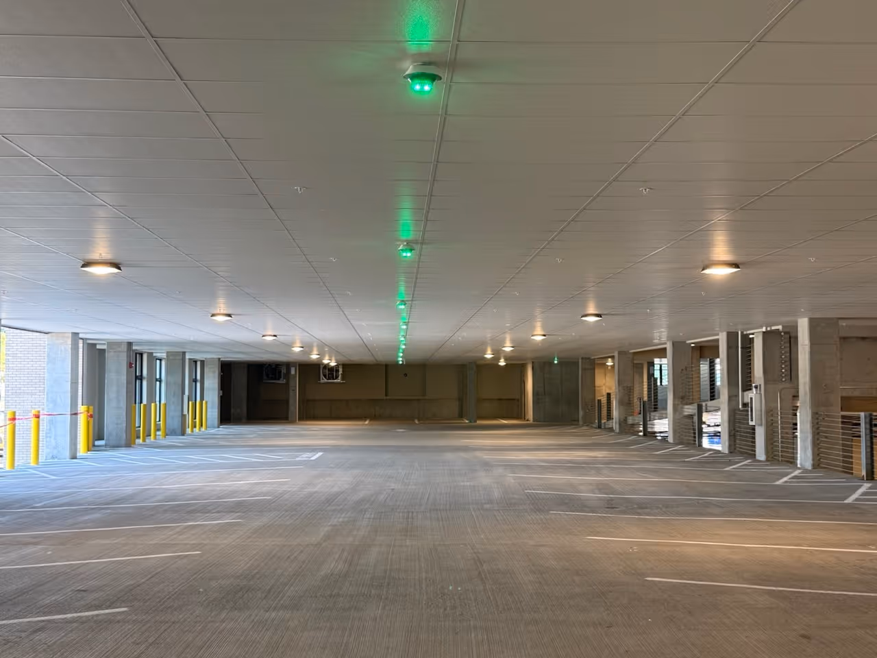 Empty multi-level parking garage with ceiling lights and green sensor lights above spaces.