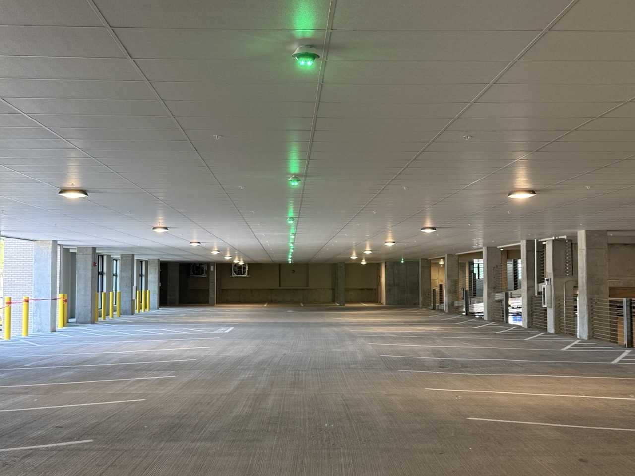 Empty multi-level parking garage with ceiling lights and green sensor lights above spaces.