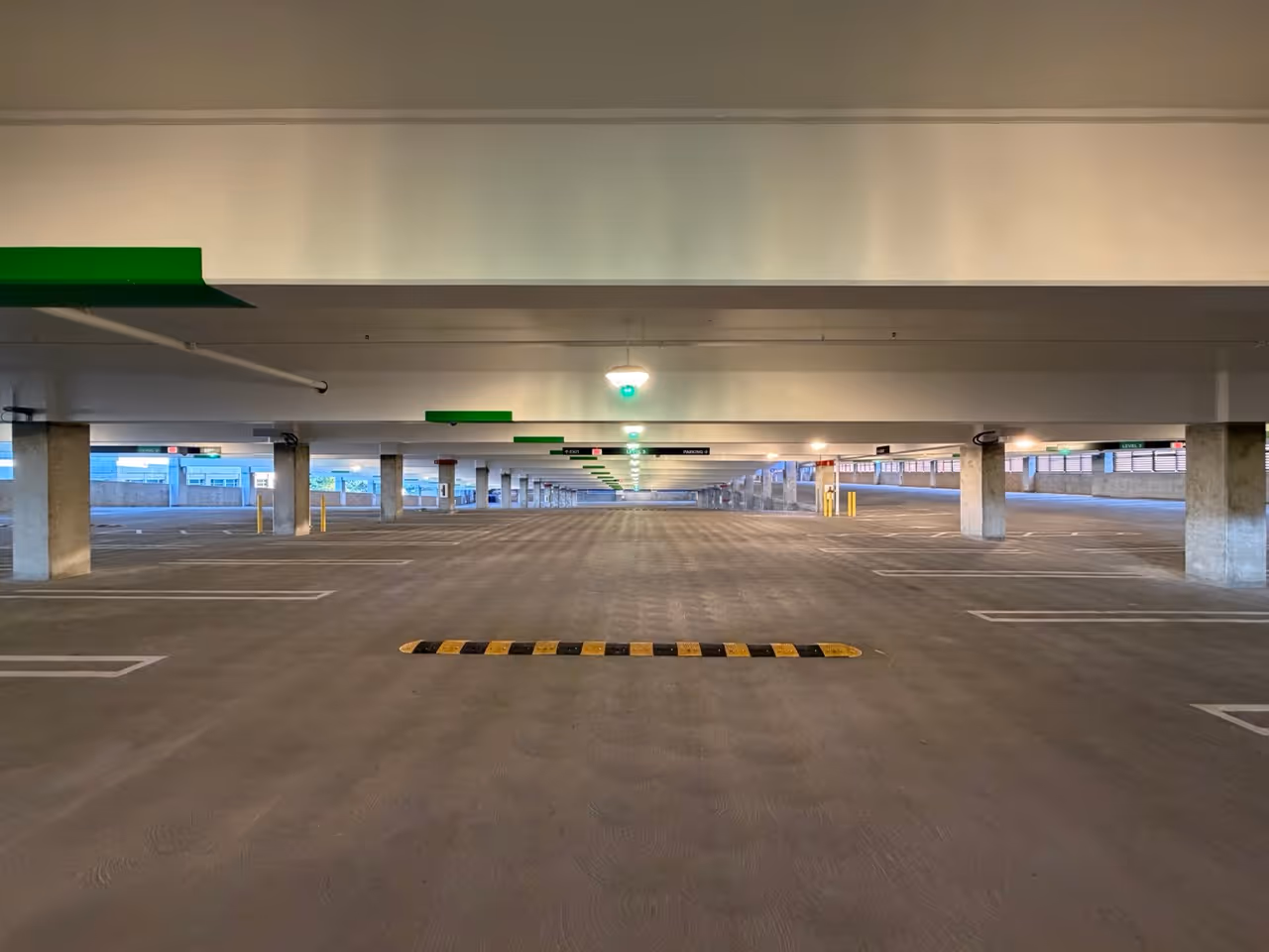Empty indoor multi-level parking garage with concrete pillars and green exit signs visible.