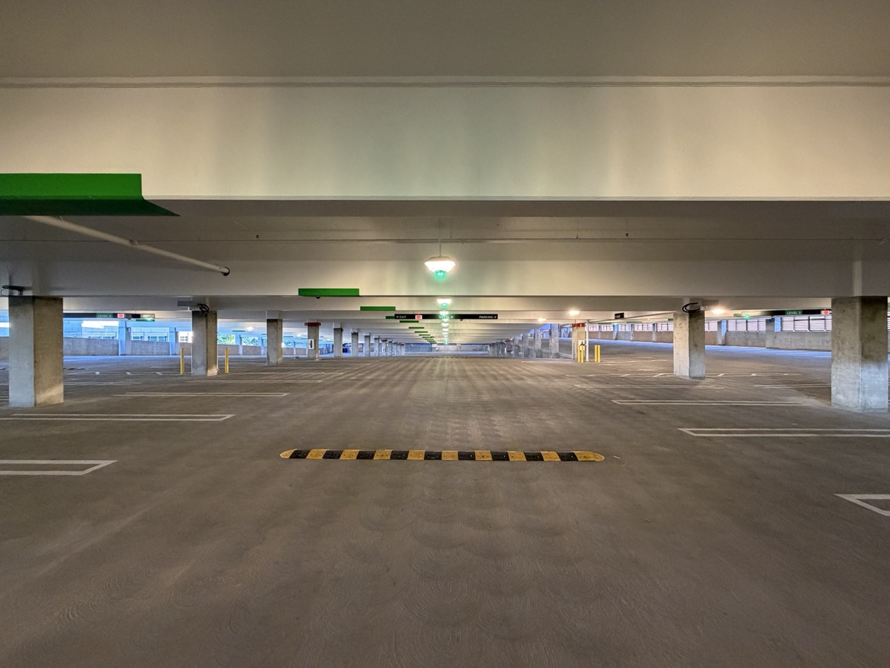Empty indoor multi-level parking garage with concrete pillars and green exit signs visible.