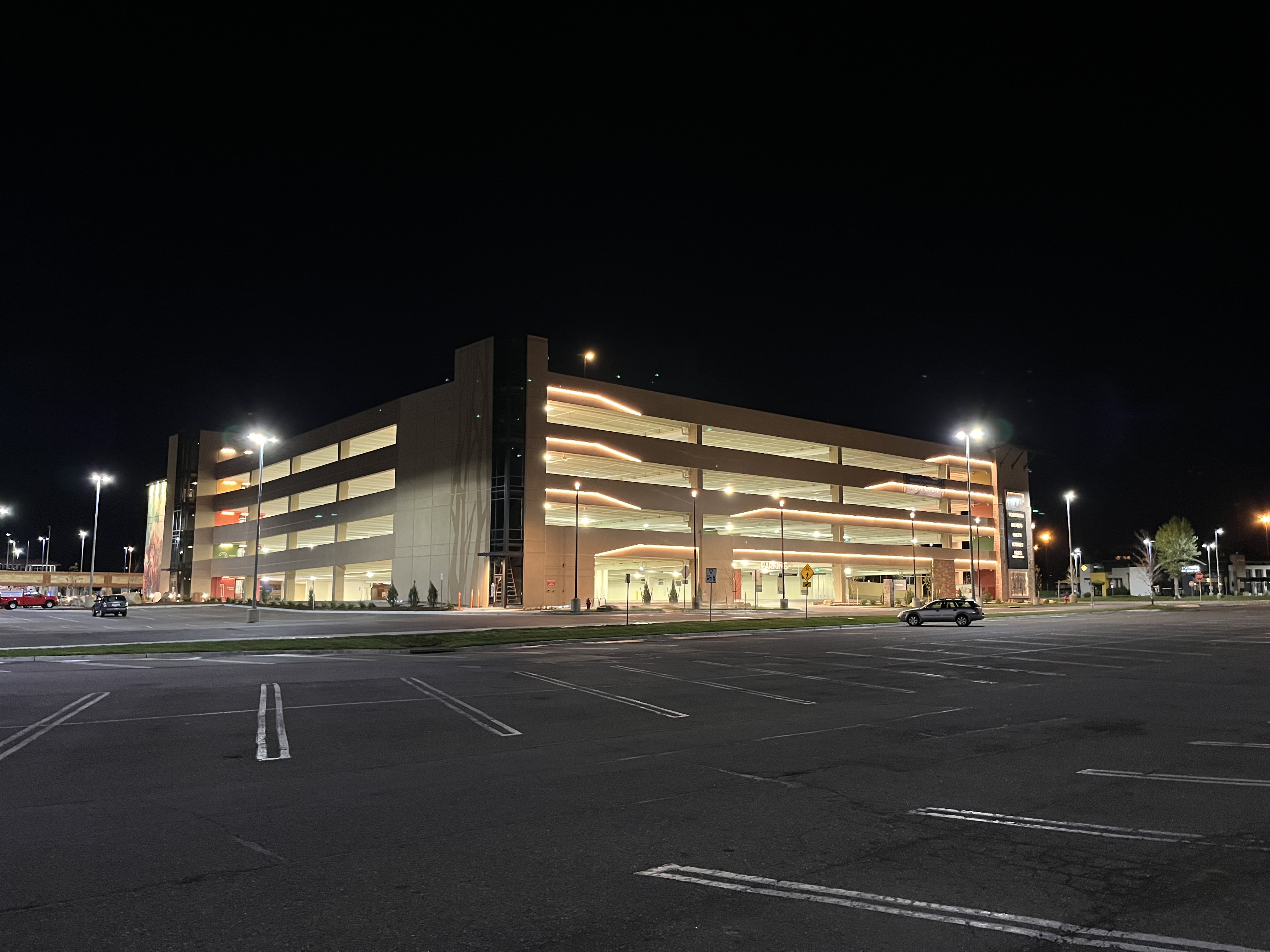 Illuminated multi-level parking garage at night with mostly empty surrounding parking lot.