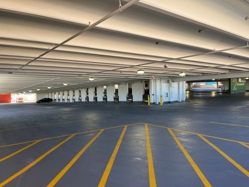 Empty indoor parking garage with yellow lines and one black car near an exit with a U-Haul truck outside.