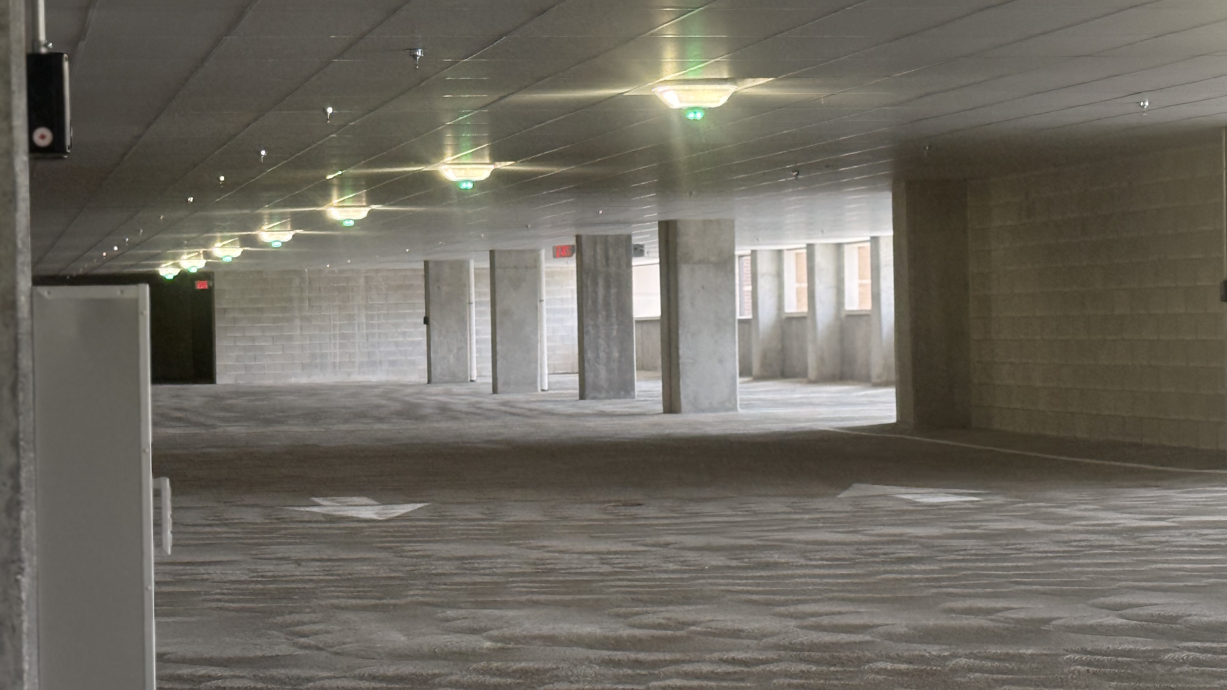 Empty multi-level parking garage with concrete pillars, ceiling lights, and directional arrows on the floor with ECO Parking EDGE Light Fixture