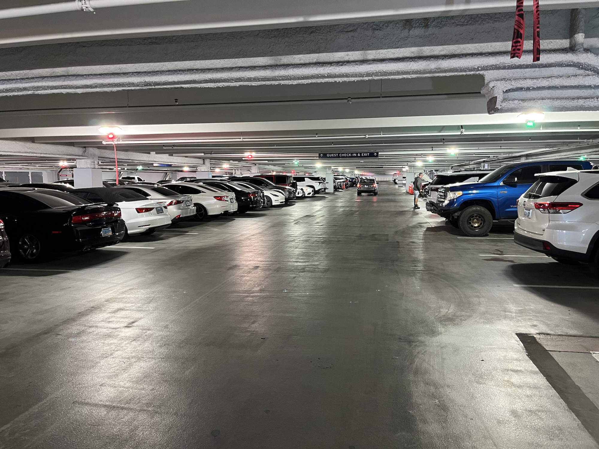 Indoor parking garage with cars lined on both sides and a person near a blue truck on right.