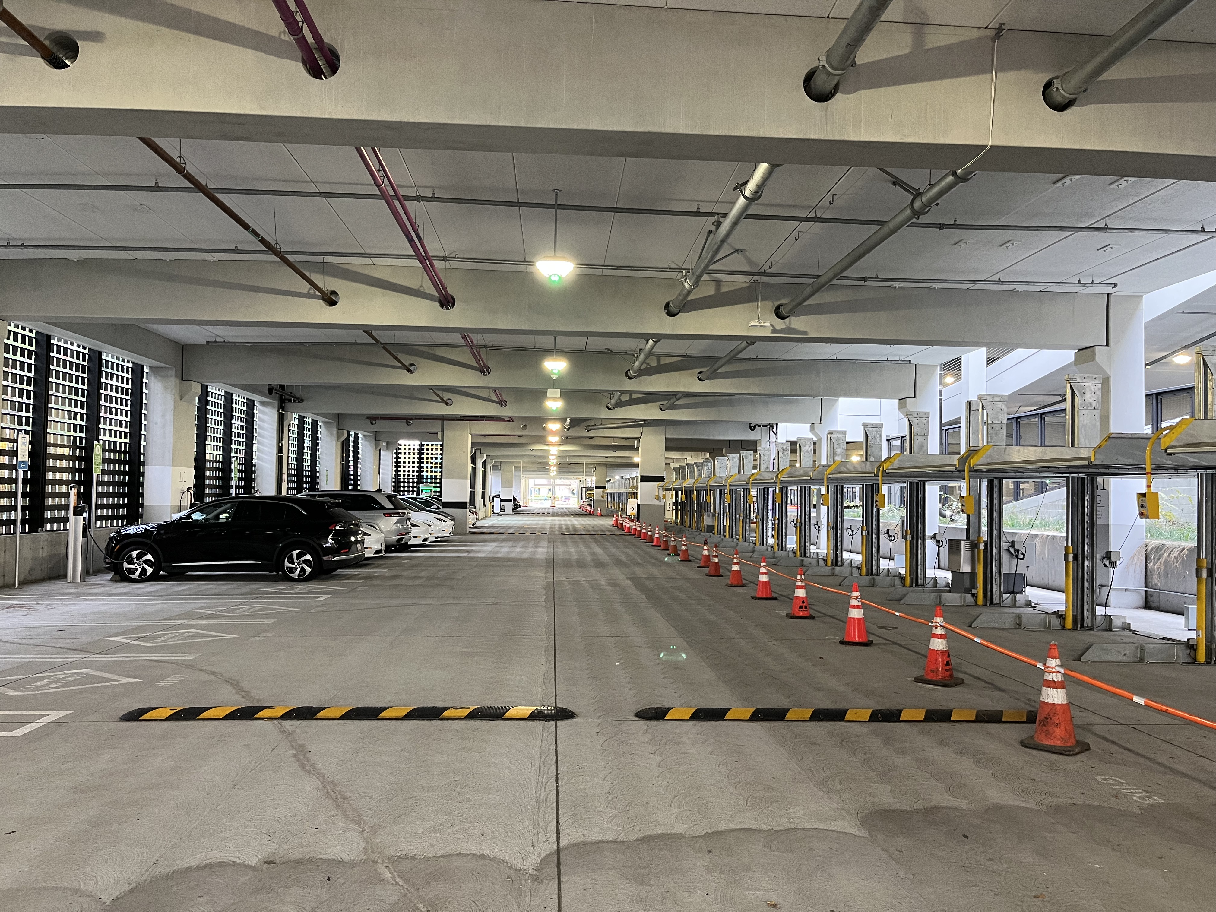 Indoor parking garage with several cars parked on the left and empty charging stations blocked by cones on the right. With ECO Edge Light Fixtures Installed