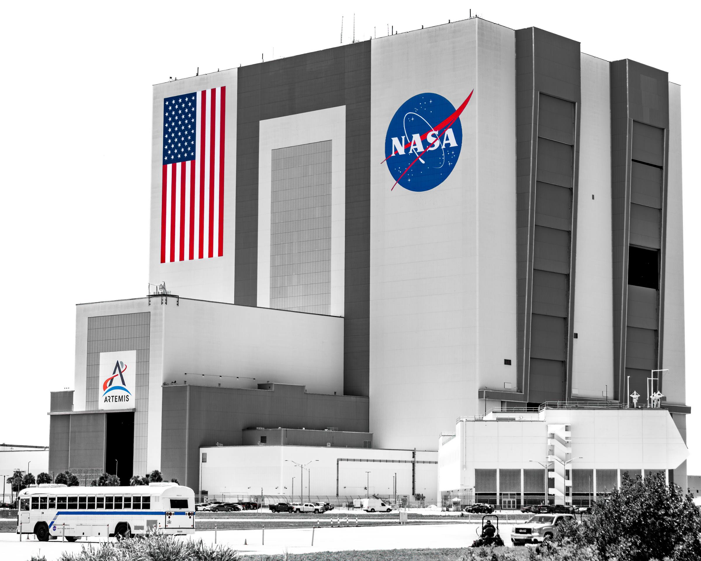 The Vehicle Assembly Building at Kennedy Space Center, desaturated except for the United States flag, the NASA insignia and the Artemis logo.