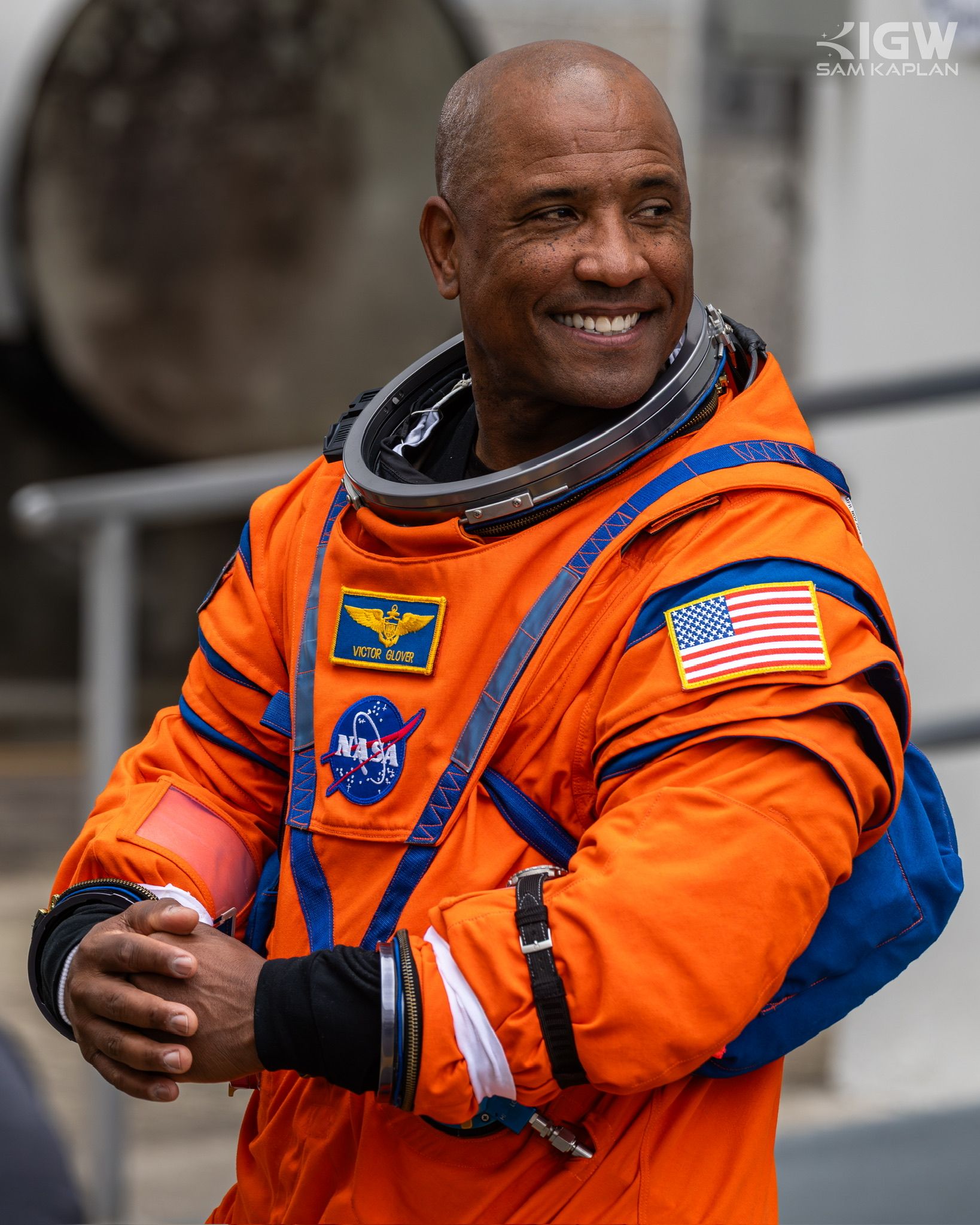 Victor Glover in the orange launch and entry suit, helmet ring open, smiling.