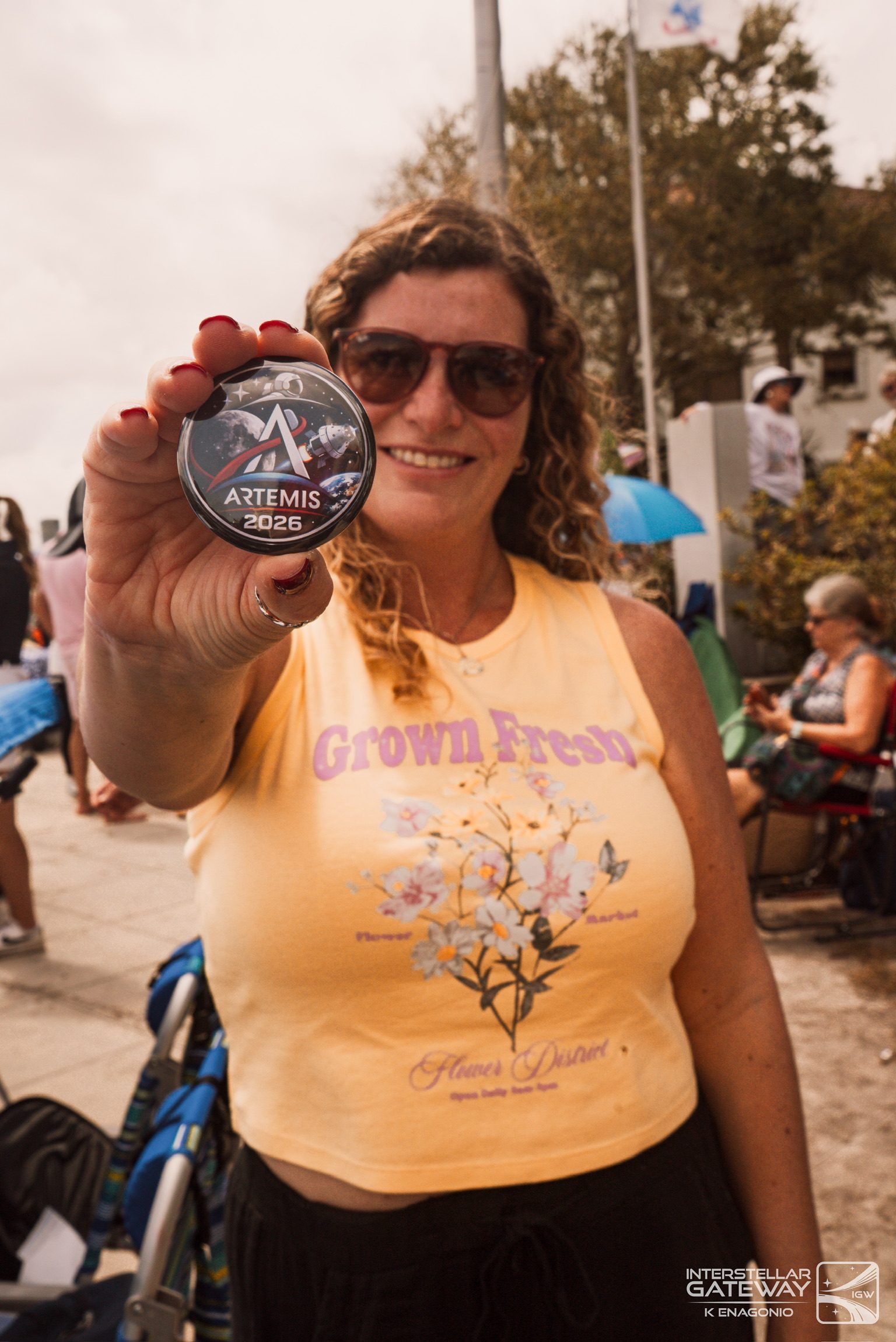 A spectator holds an Artemis medallion up toward the camera at a launch viewing site.