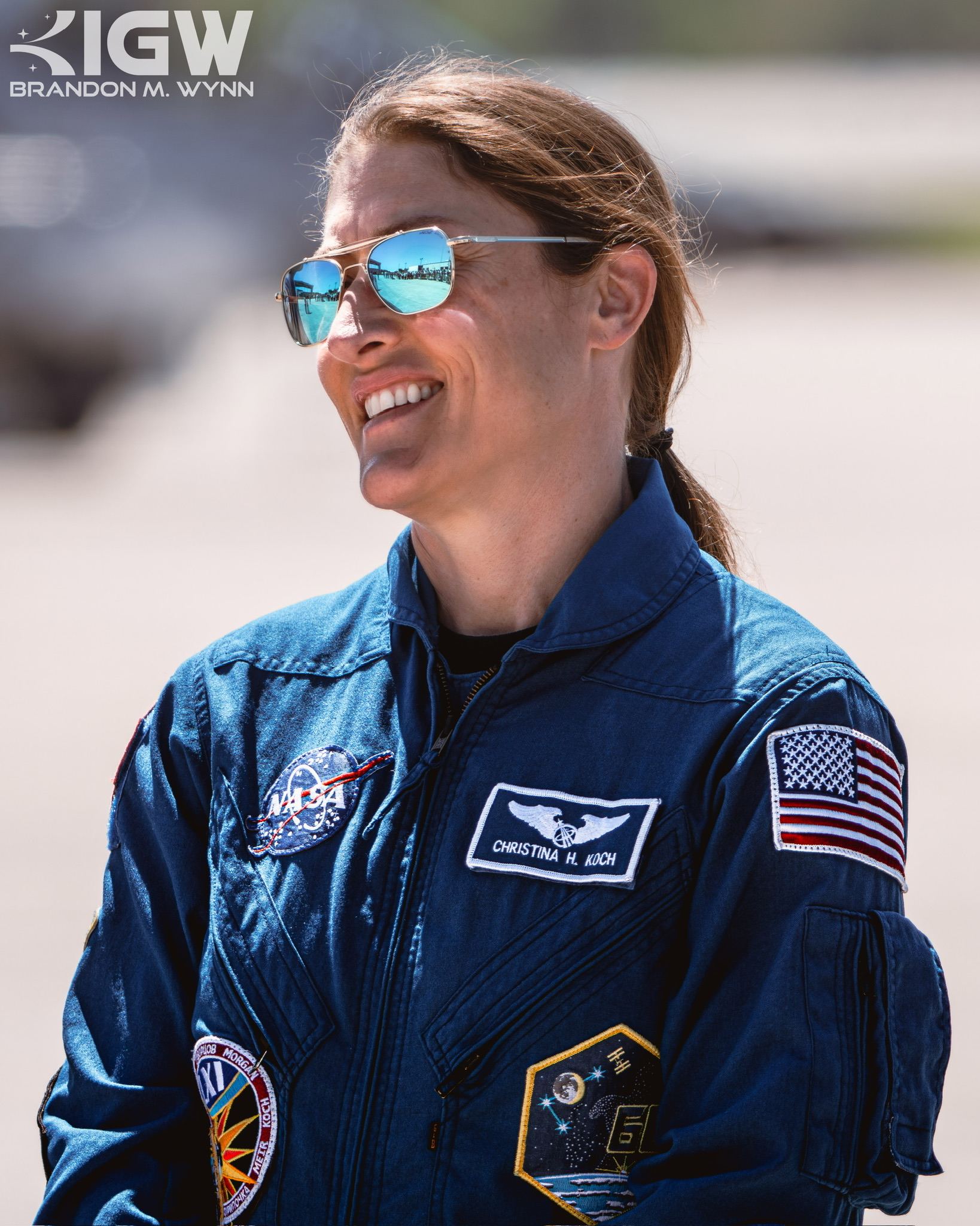 Christina Koch in a blue NASA flight suit, smiling in sunglasses.