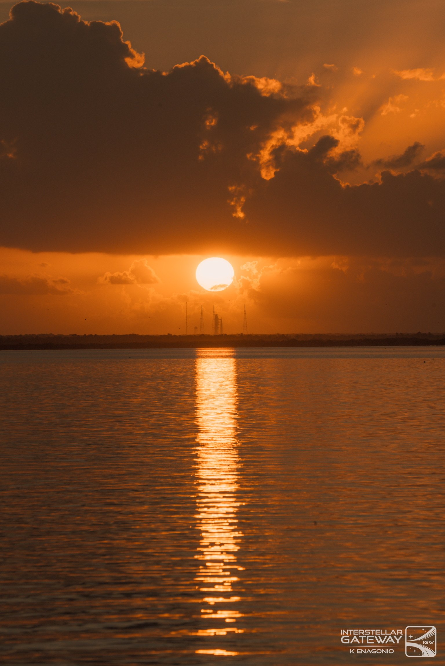 The sun rising over water beneath a bank of cloud, its reflection running toward the camera.