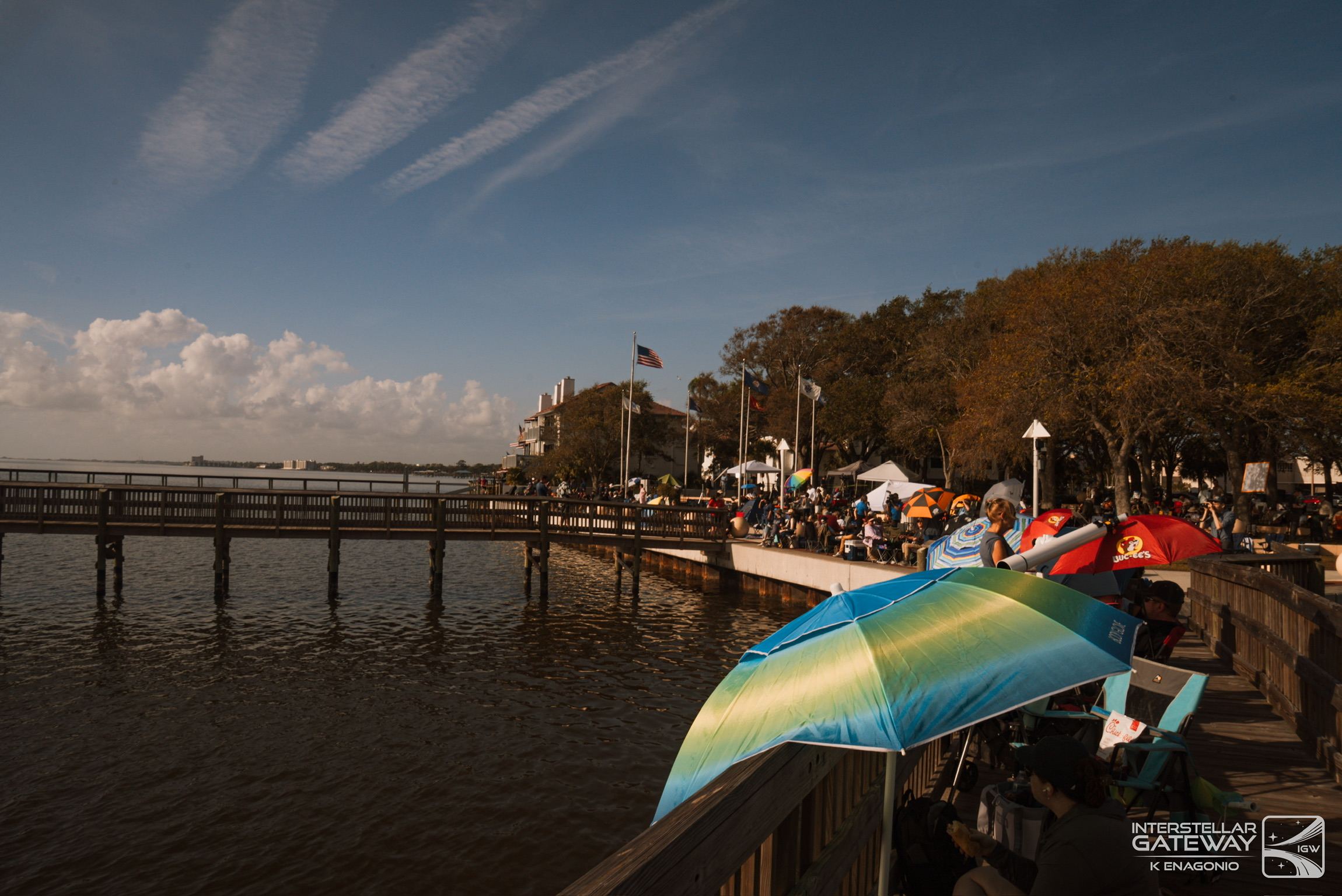 Spectators along a pier at a waterfront viewing site in late light.