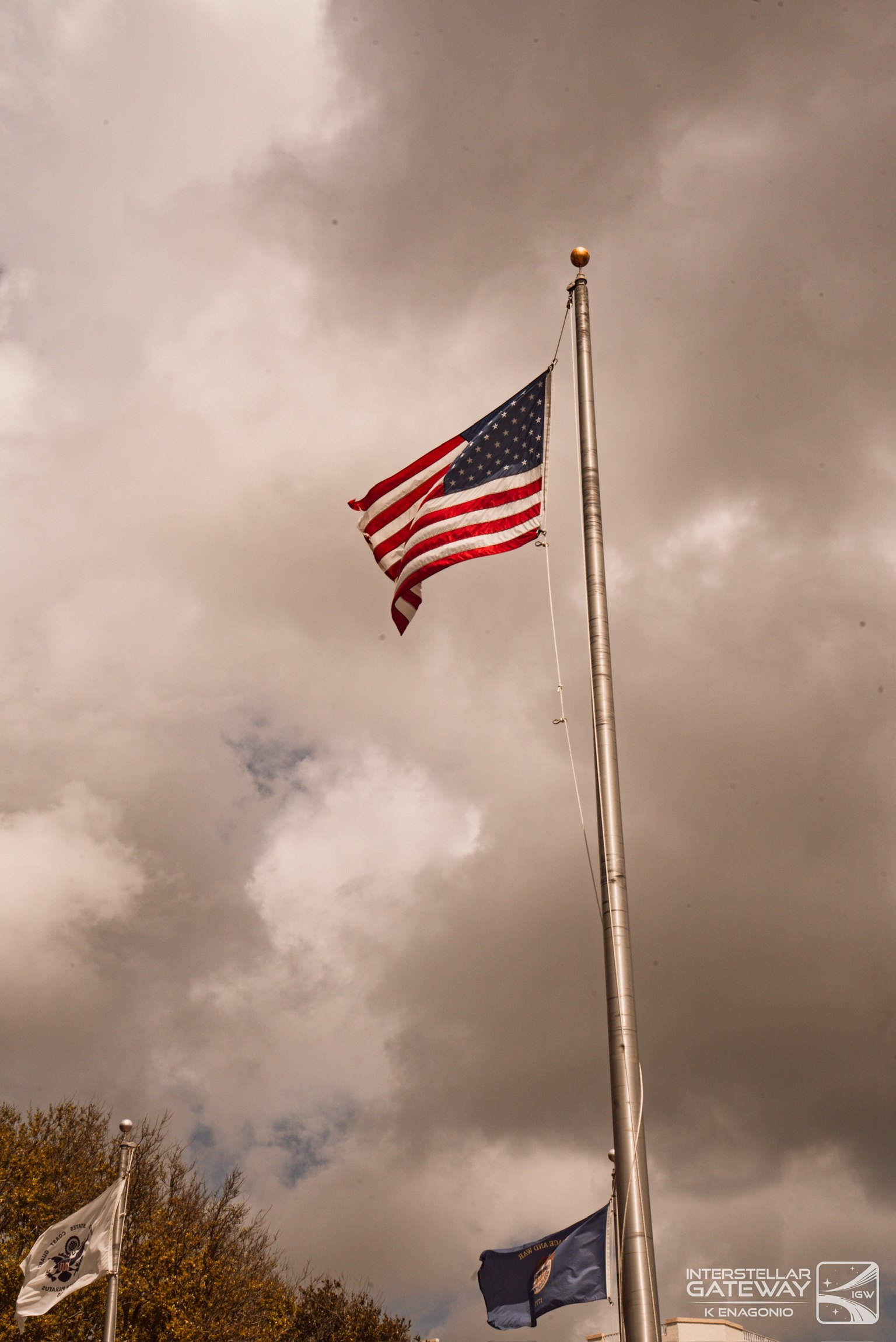A United States flag against heavy cloud, two smaller flags below it.