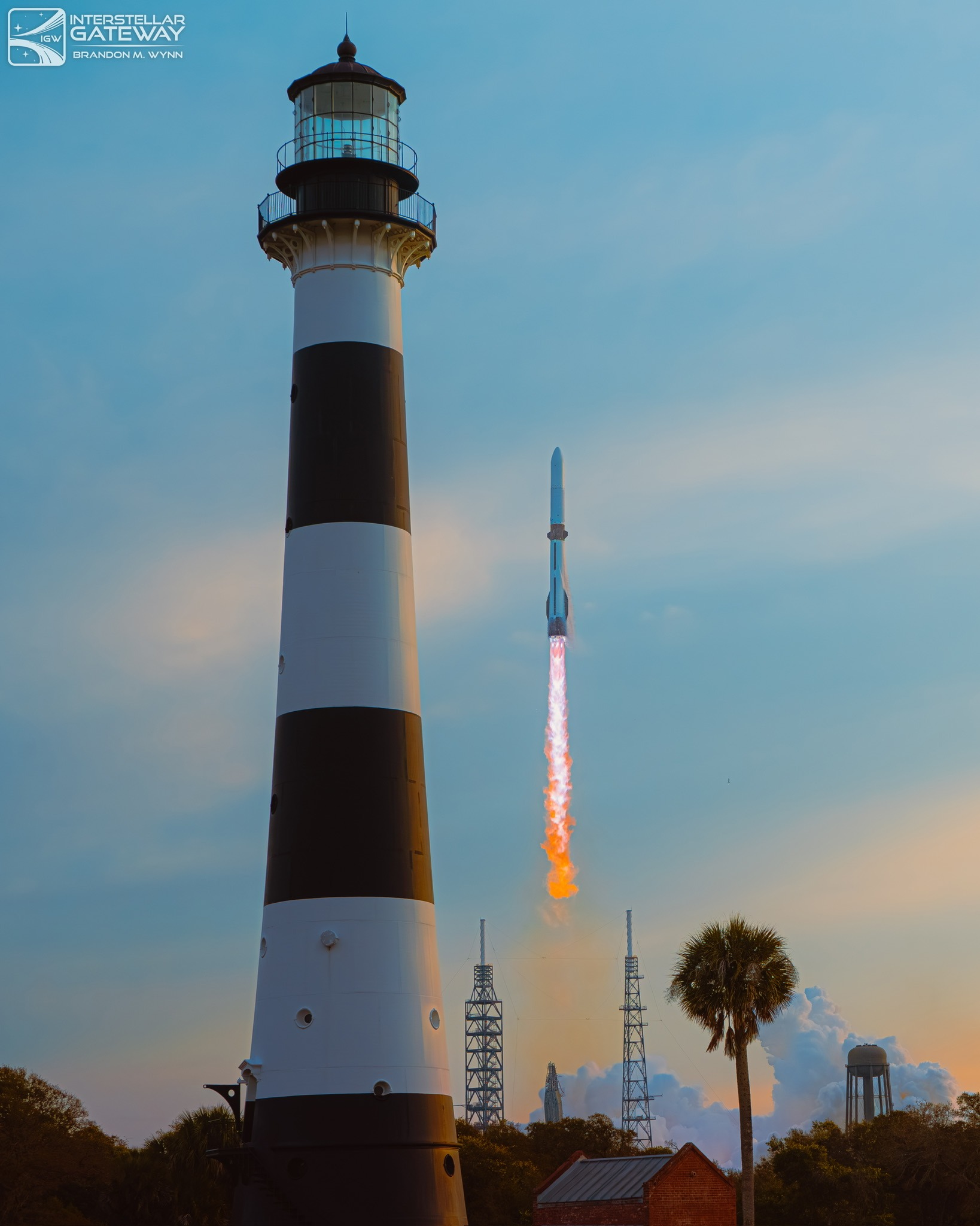 A rocket climbs on a bright plume past the black-and-white Cape Canaveral Lighthouse.