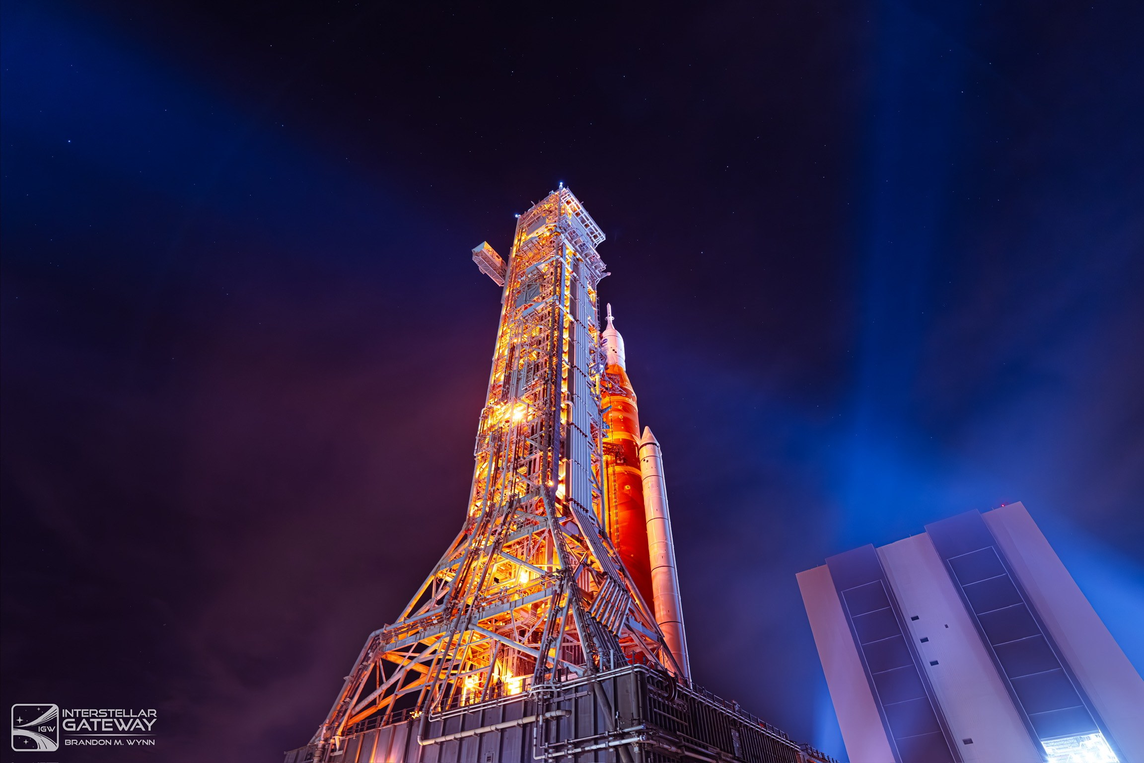 The Space Launch System on its mobile launcher at night under a deep blue sky.