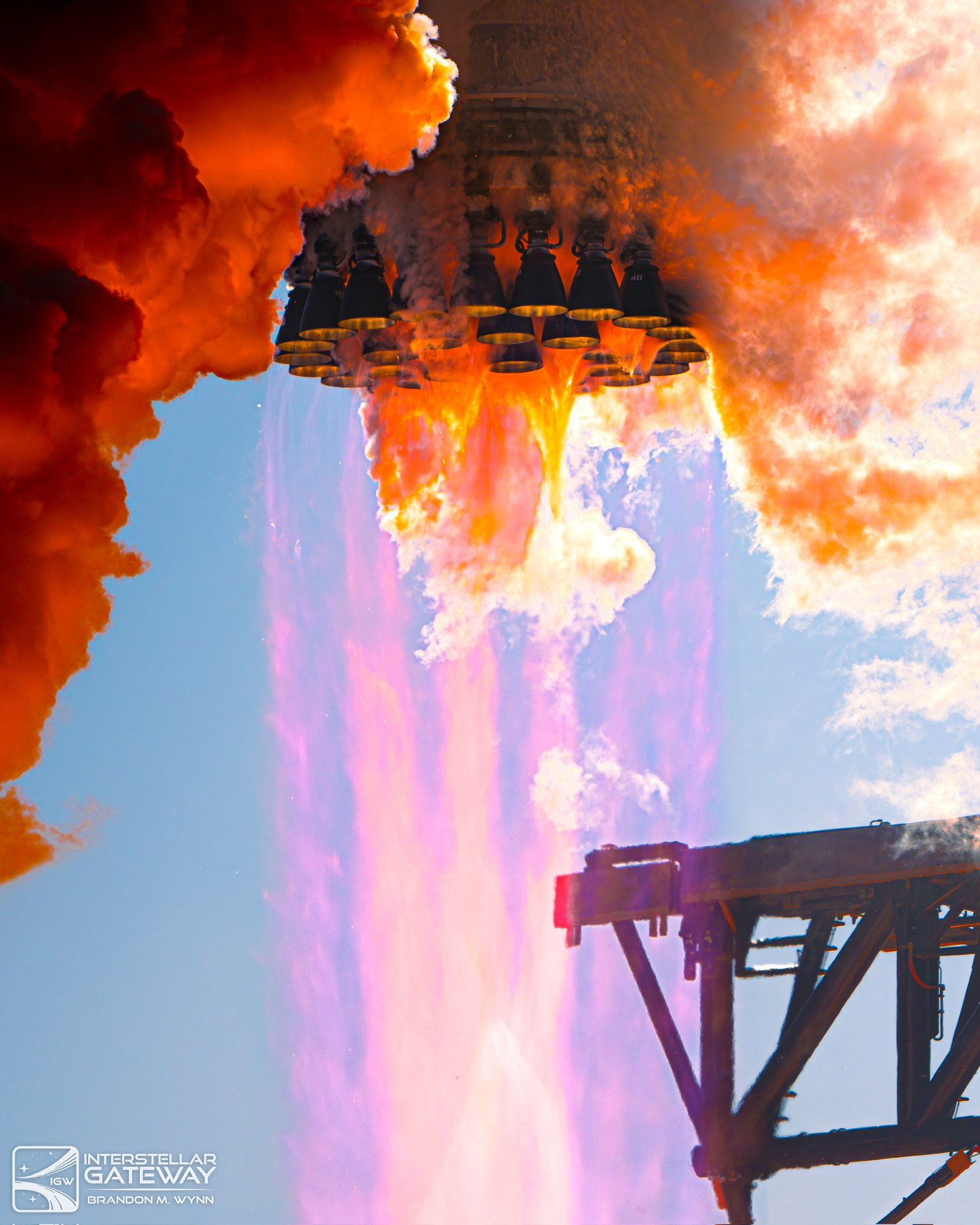The engines of a Super Heavy booster firing, seen from below against cloud.