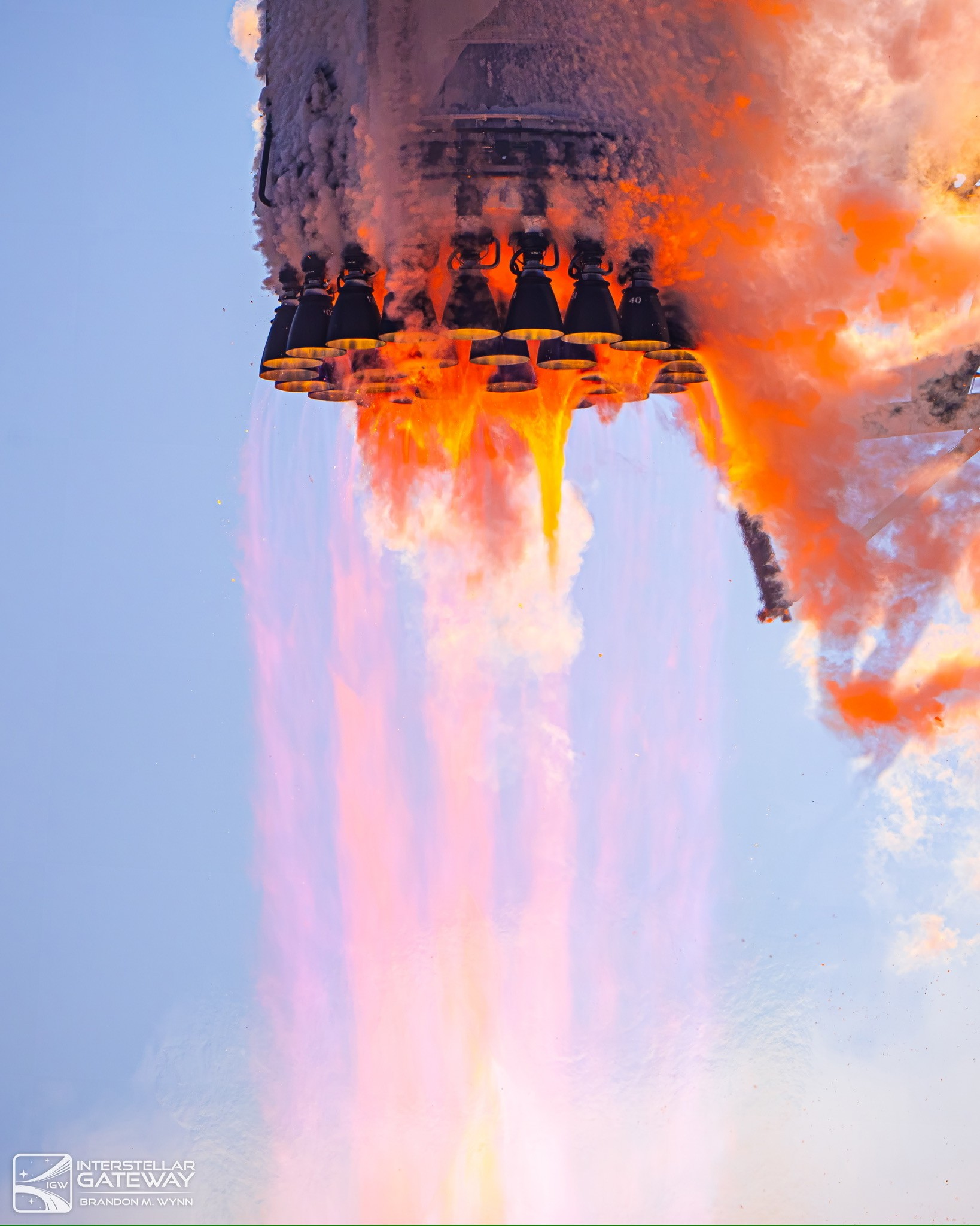 A Super Heavy booster with its engines lit, exhaust wrapped around the aft end.