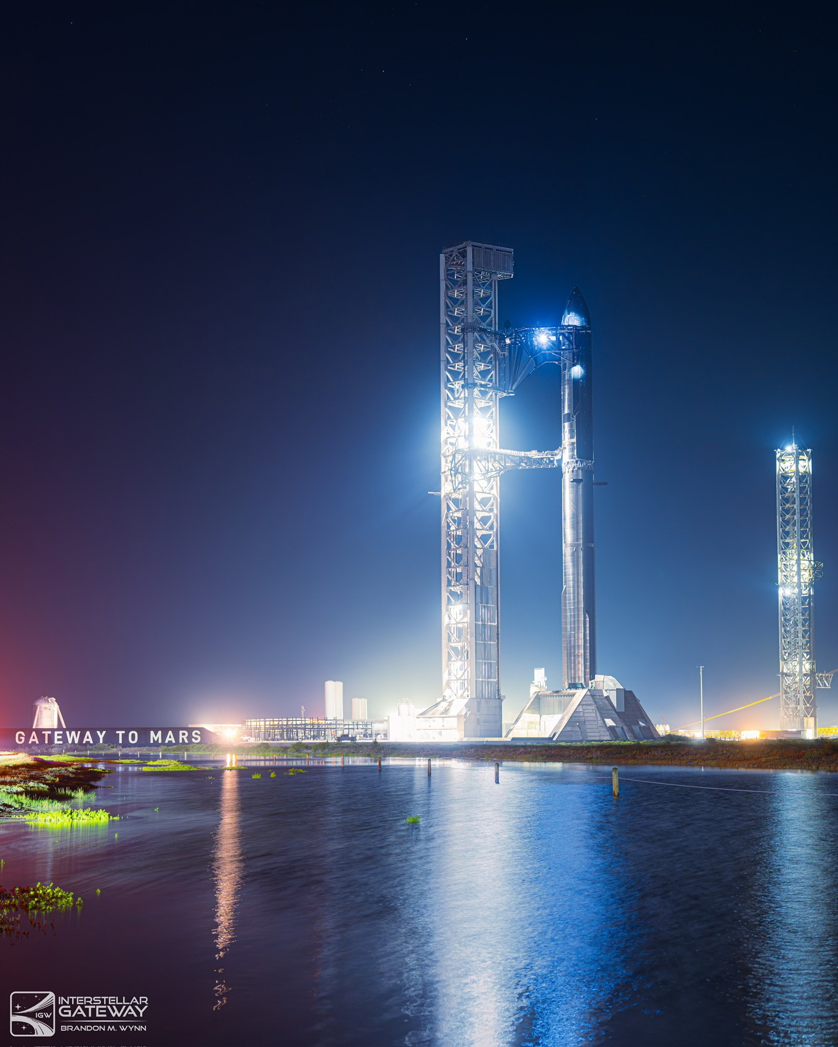 Starbase at night: the launch tower and pad floodlit, the "Gateway to Mars" sign lit in the foreground.