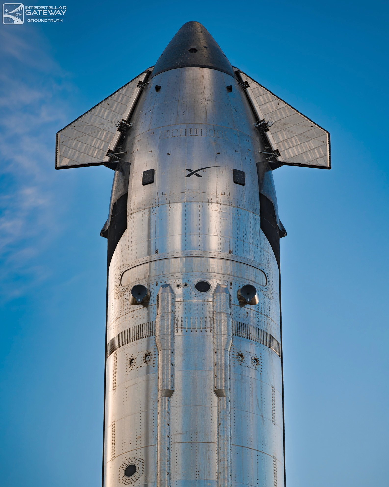 Starship's nose and forward flaps from below, the heat-shield side dark.