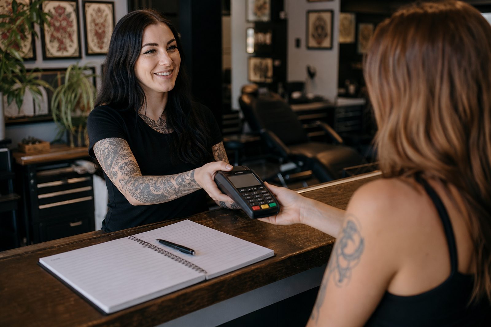 Tattoo shop receptionist handing a client a card terminal to pay a booking deposit at the front desk