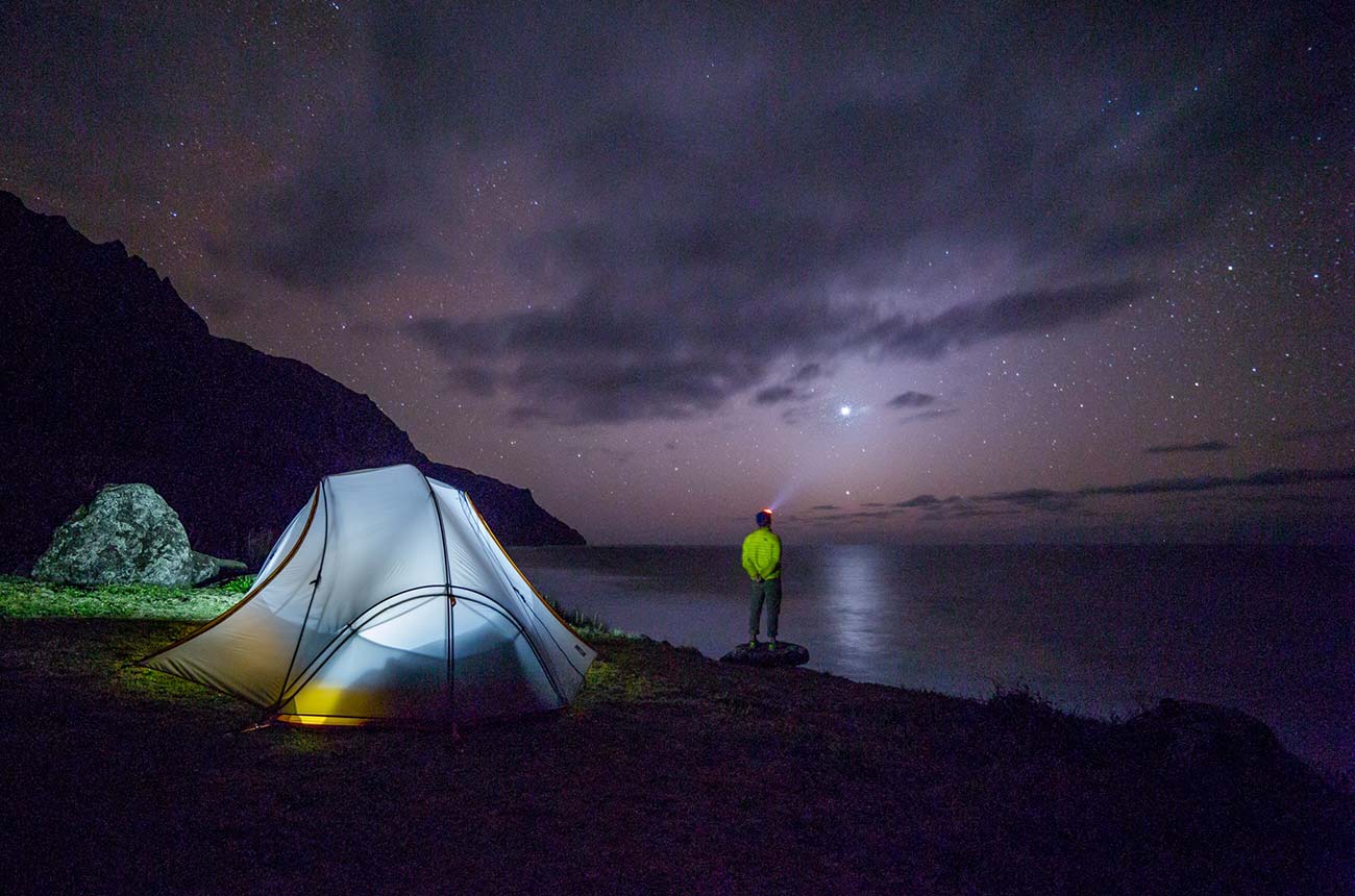 a man standing next to a tent under a night sky