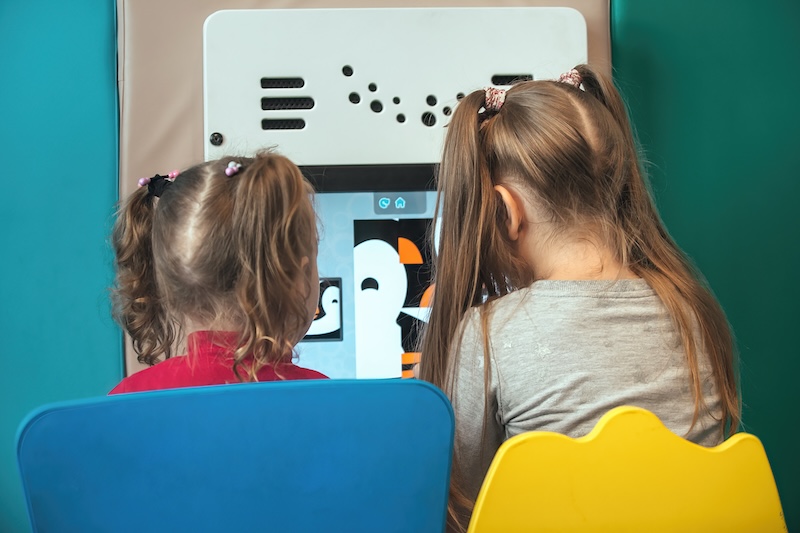 Two young female students in a classroom, sitting in chairs looking at computer screen with a stem project on it.