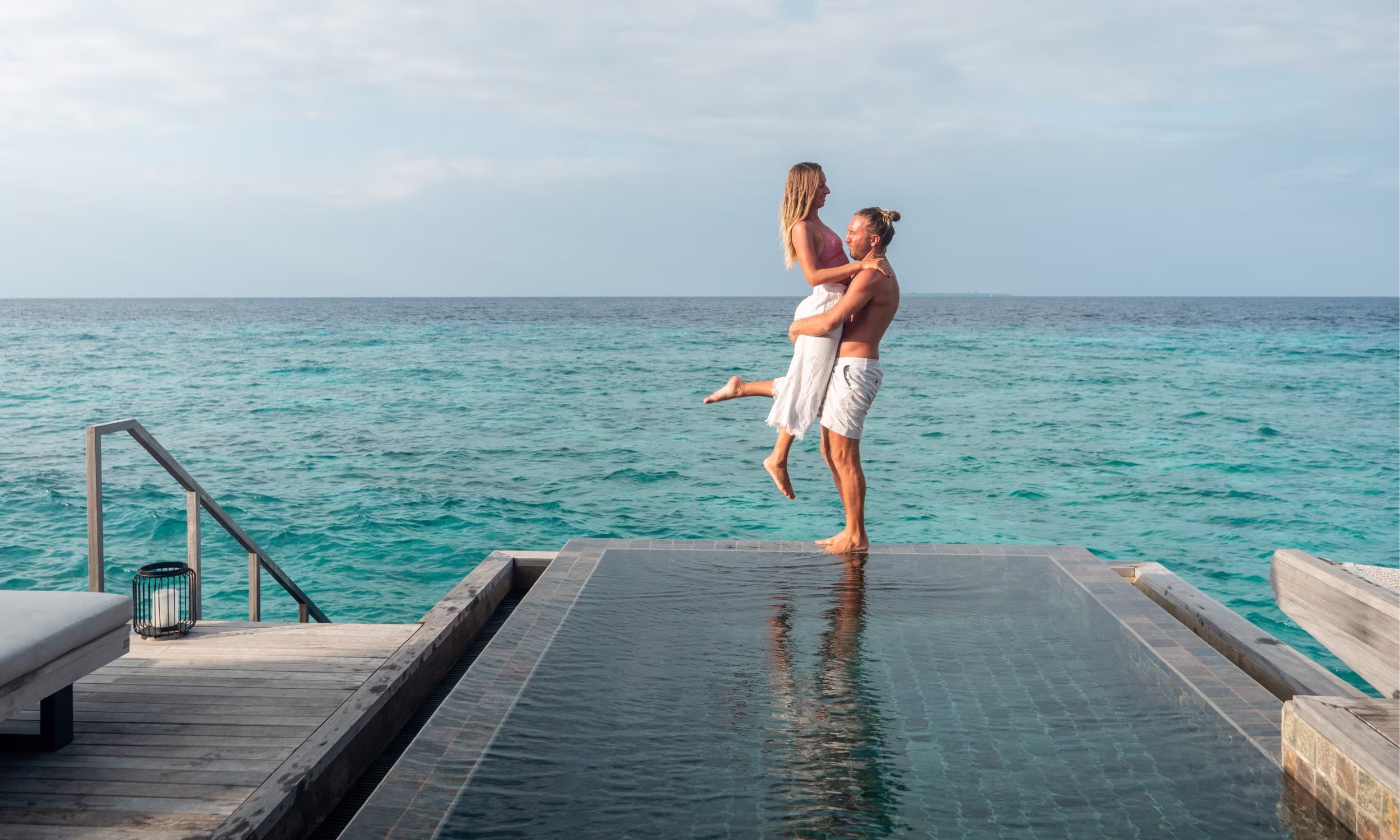 Honeymoon couple hugging by the ocean in an overwater villa in the Maldives.