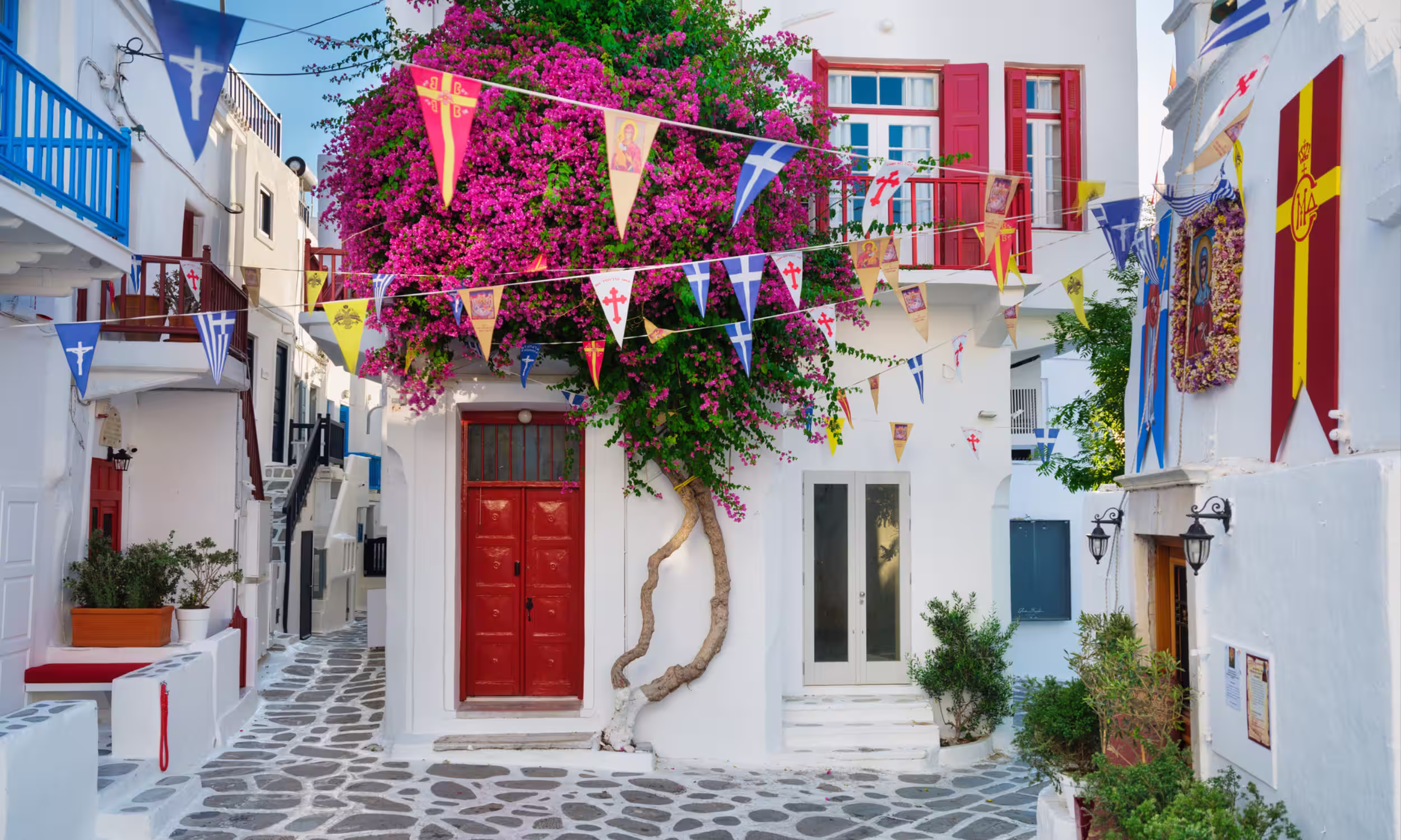Charming street in Mykonos with white houses, flowers, and colorful flags. 