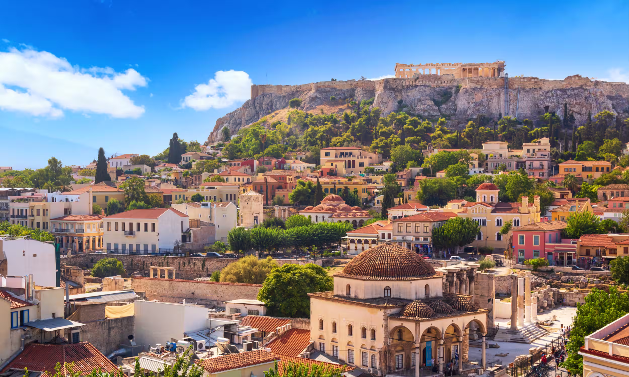 View of Athens with the Acropolis and city rooftops under a clear blue sky.
