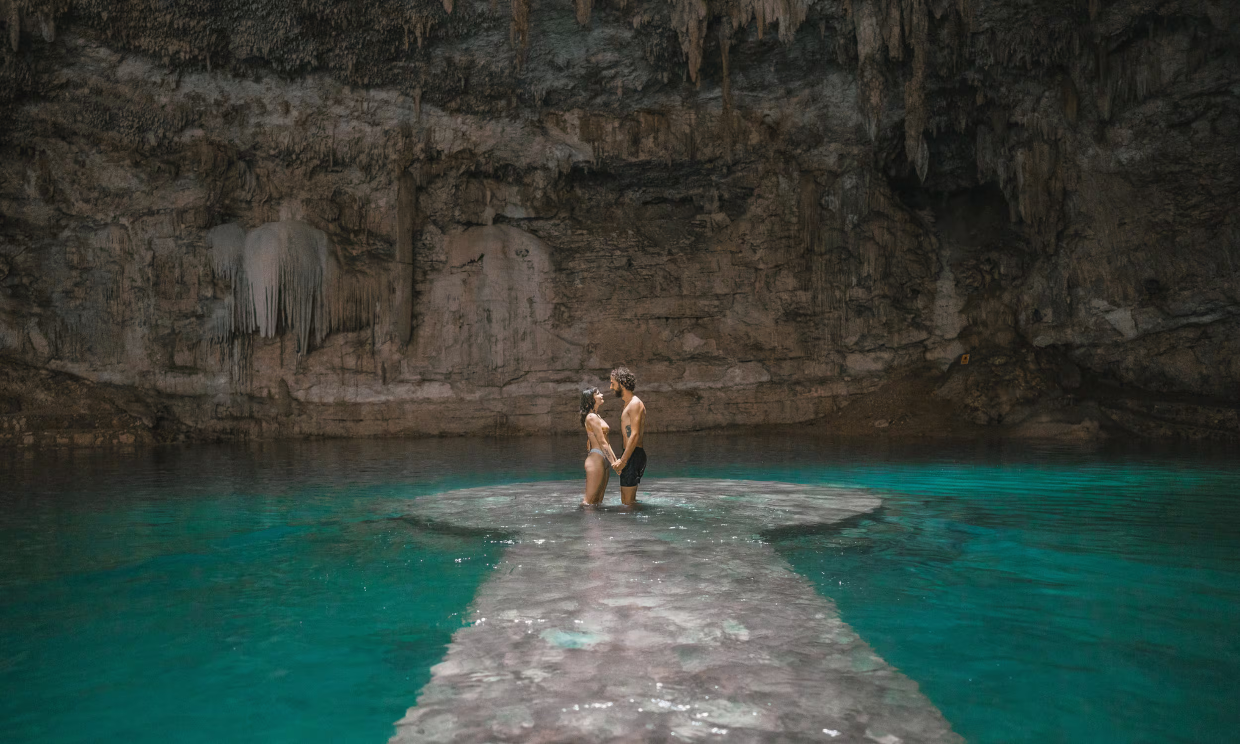Honeymoon couple standing hand in hand in a crystal-clear cenote inside a natural cave in Mexico. 