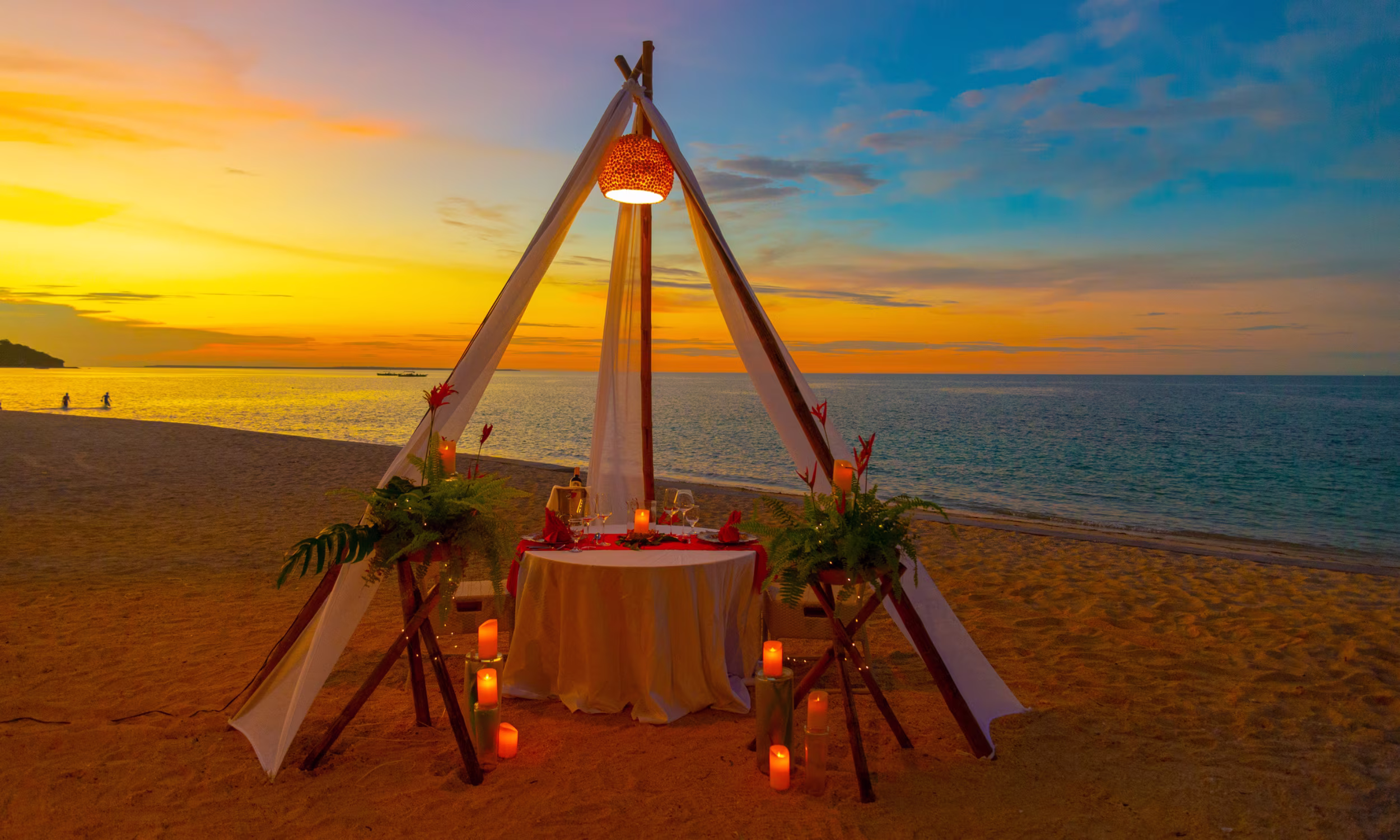 Romantic beach dinner at sunset in Mexico with candles and boho-chic setup. 